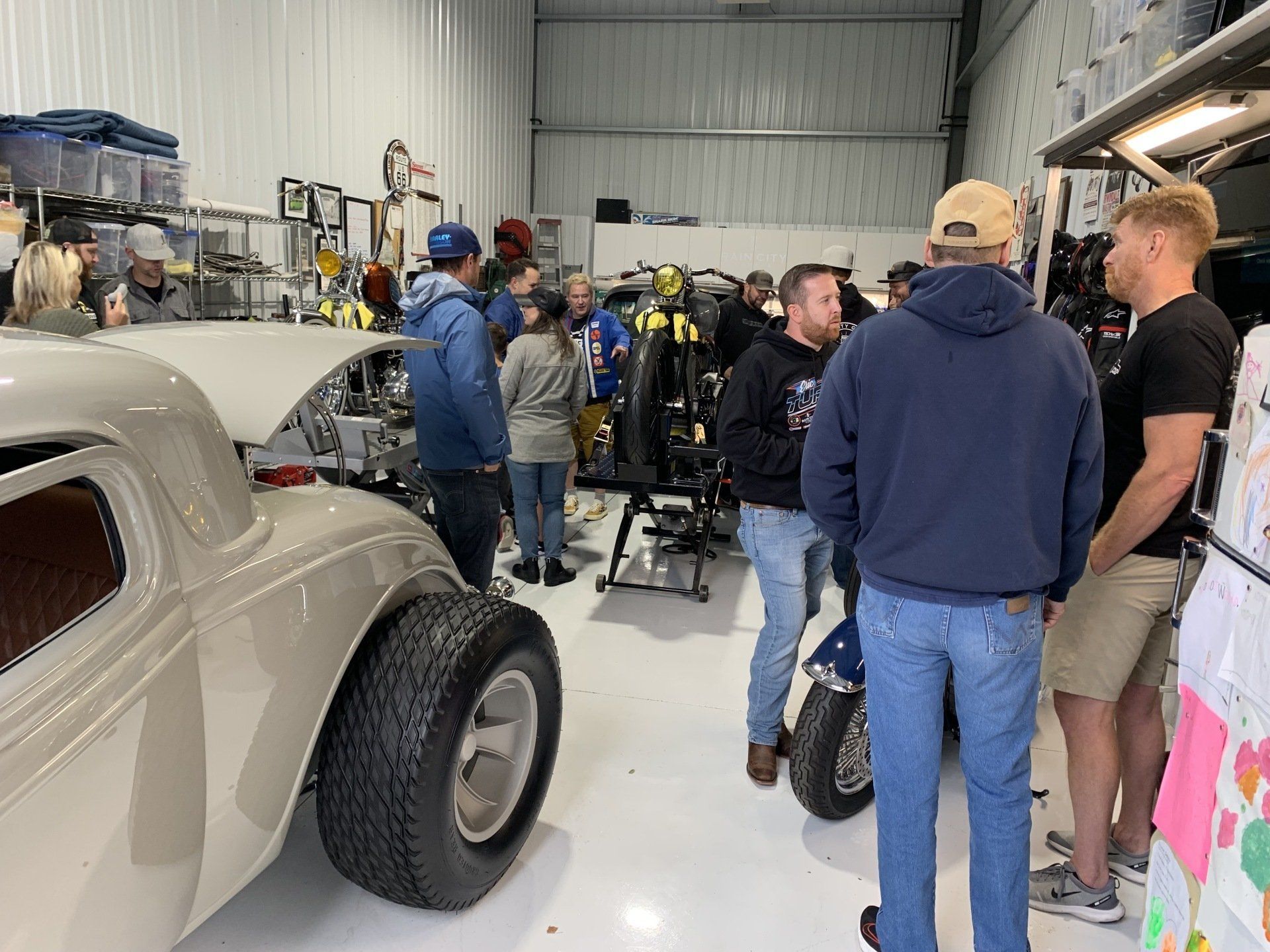 People gathered in a workshop around a classic car during what looks like an auto event