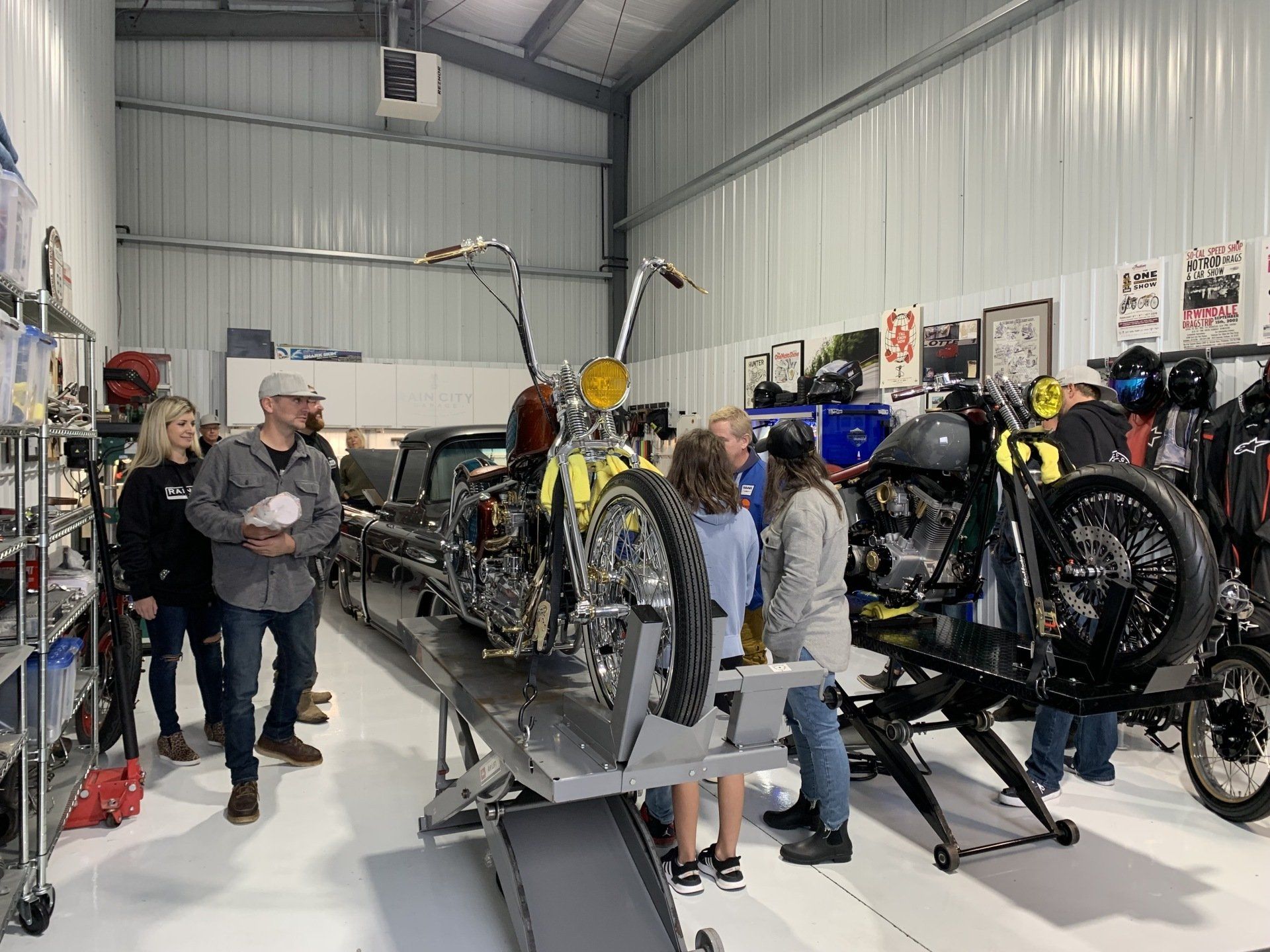 People examining custom motorcycles inside a bright workshop, with several bikes on display.