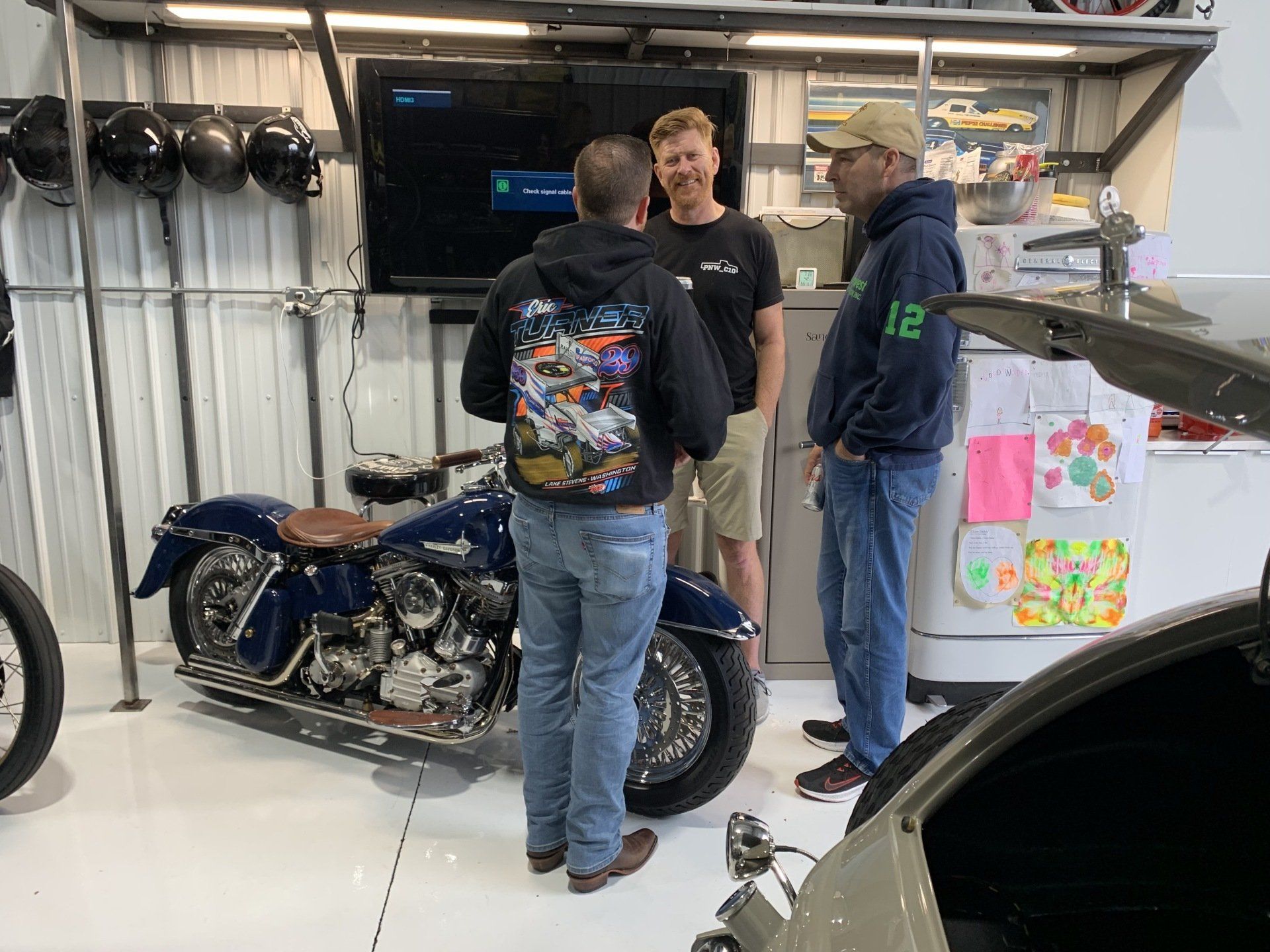 Three people chatting beside a blue motorcycle in a garage workshop