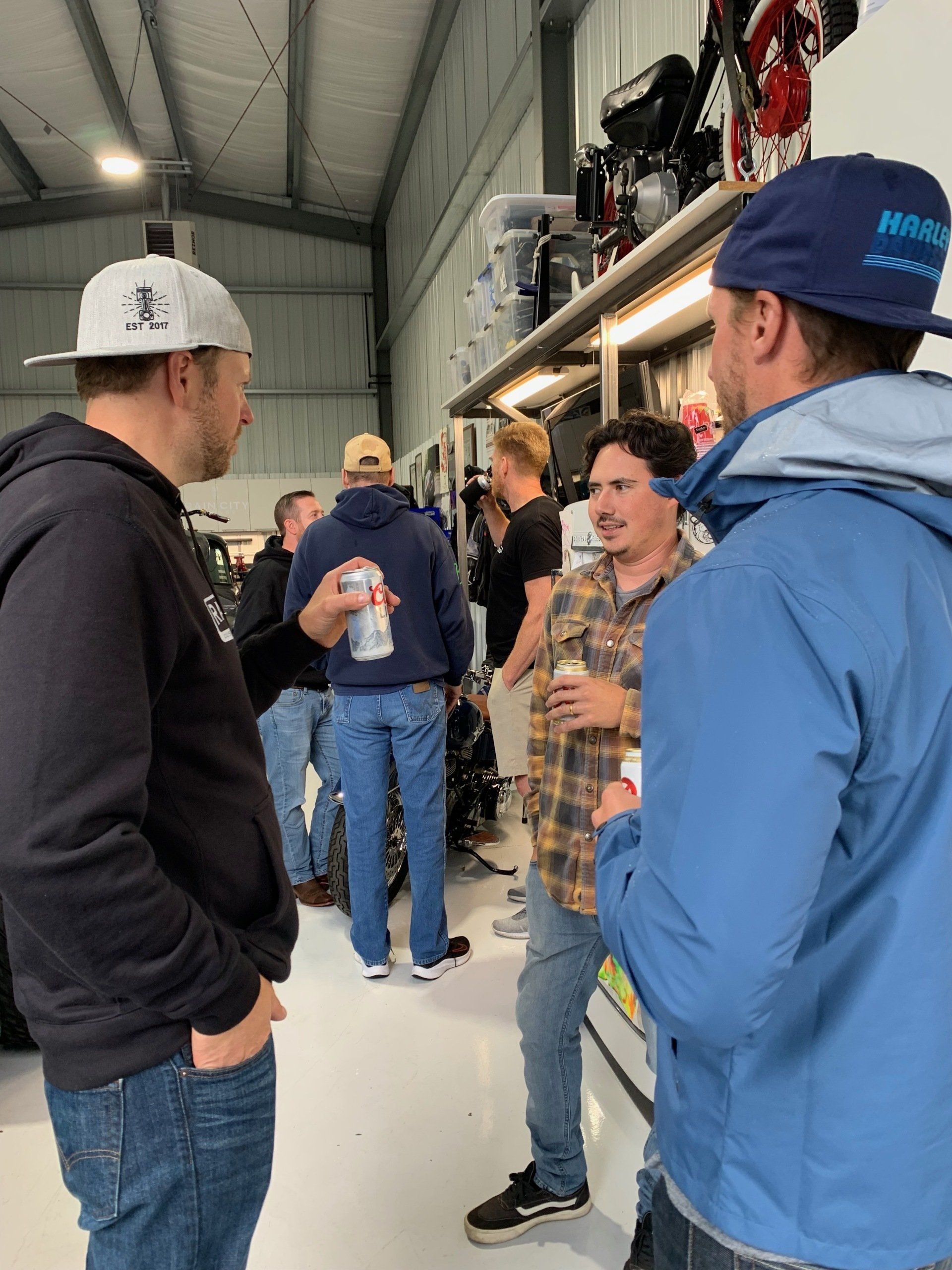 People chatting in a workshop with high shelves and industrial equipment.