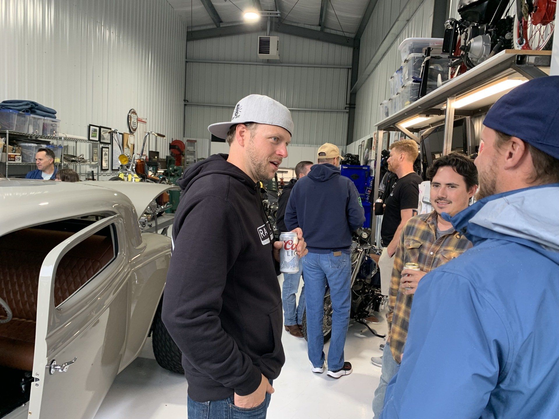 People talking in a workshop beside a car body and tools on shelves