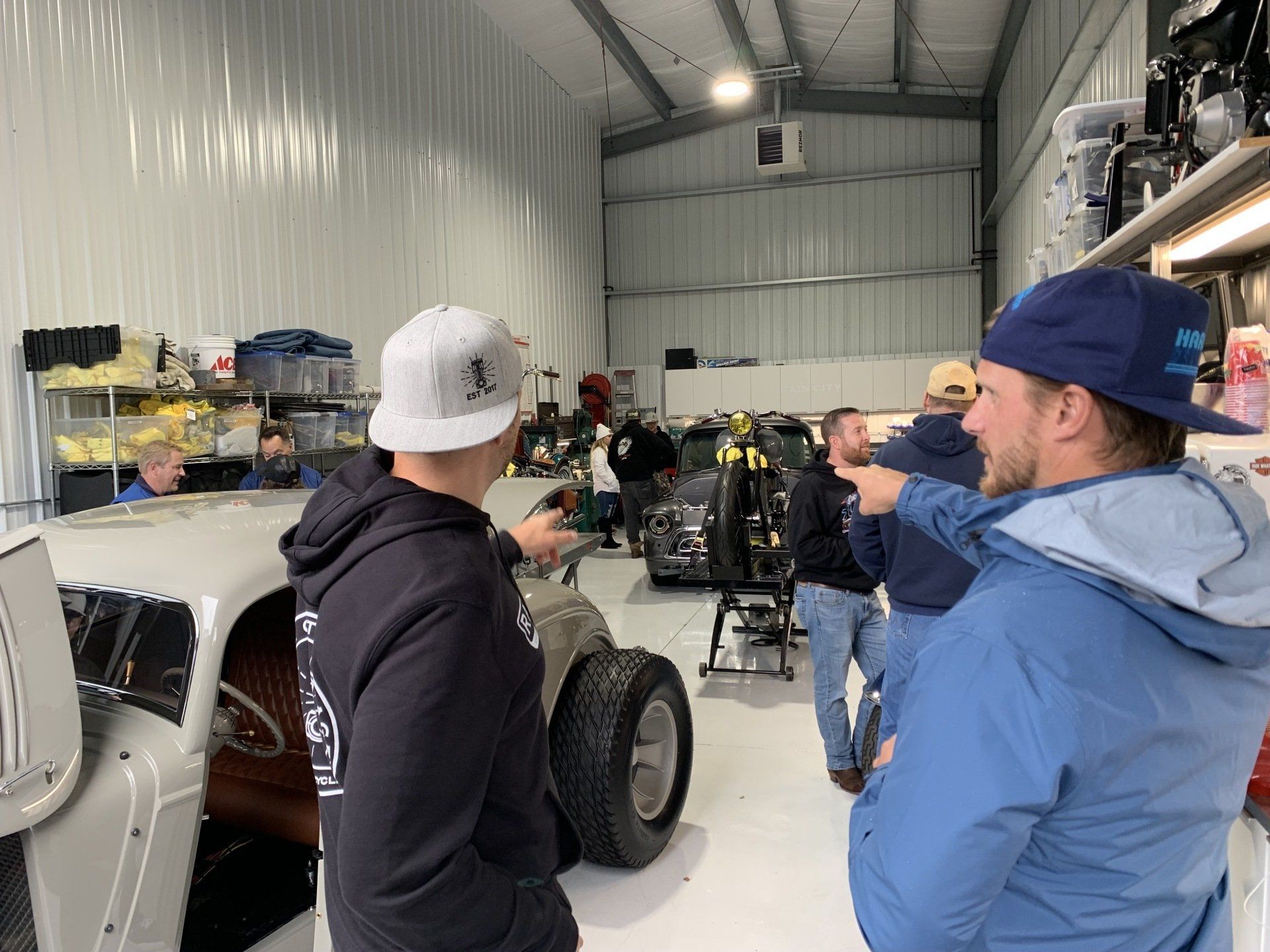 Three people in a workshop, one pointing toward a partially assembled off-road vehicle.