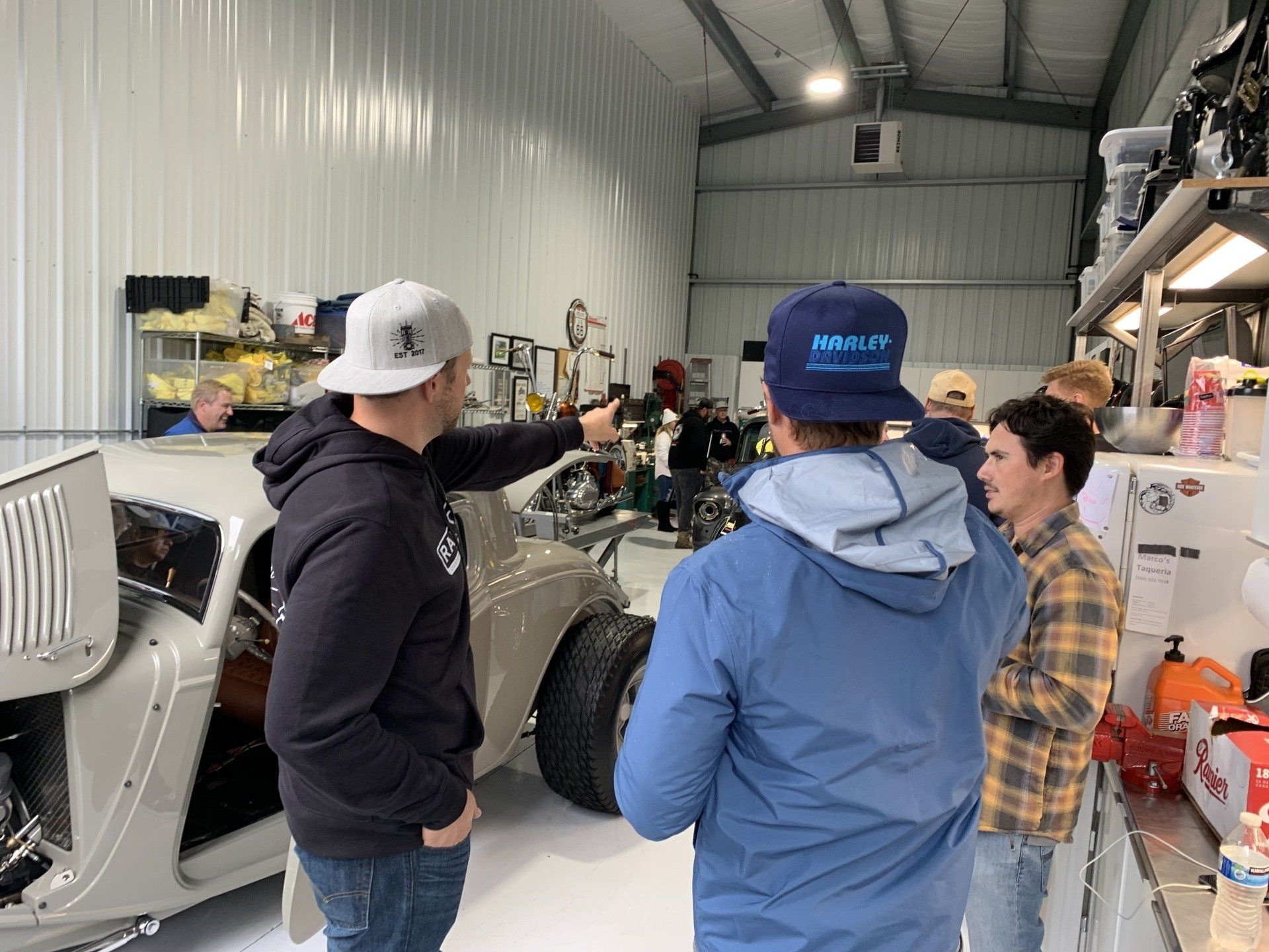 Three people talking beside a silver car in a workshop garage