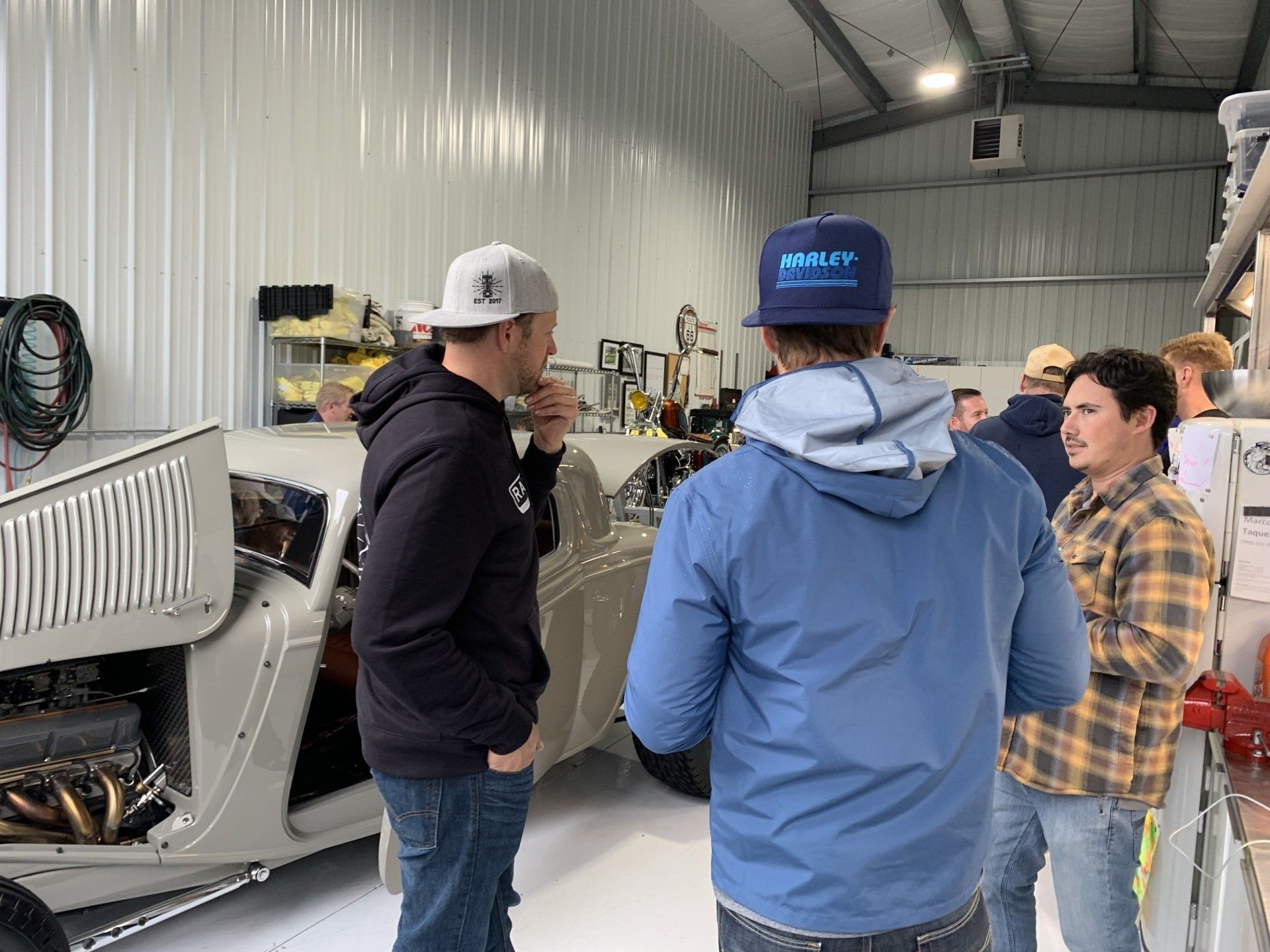 Three people in a workshop discussing a machine inside an industrial garage.