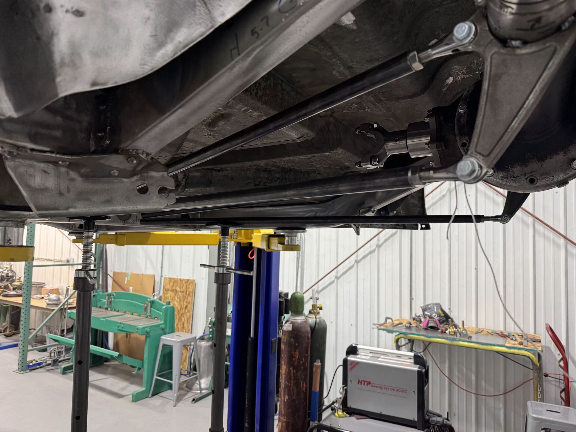 Underside of a car on a lift in an auto repair shop with tools and equipment nearby