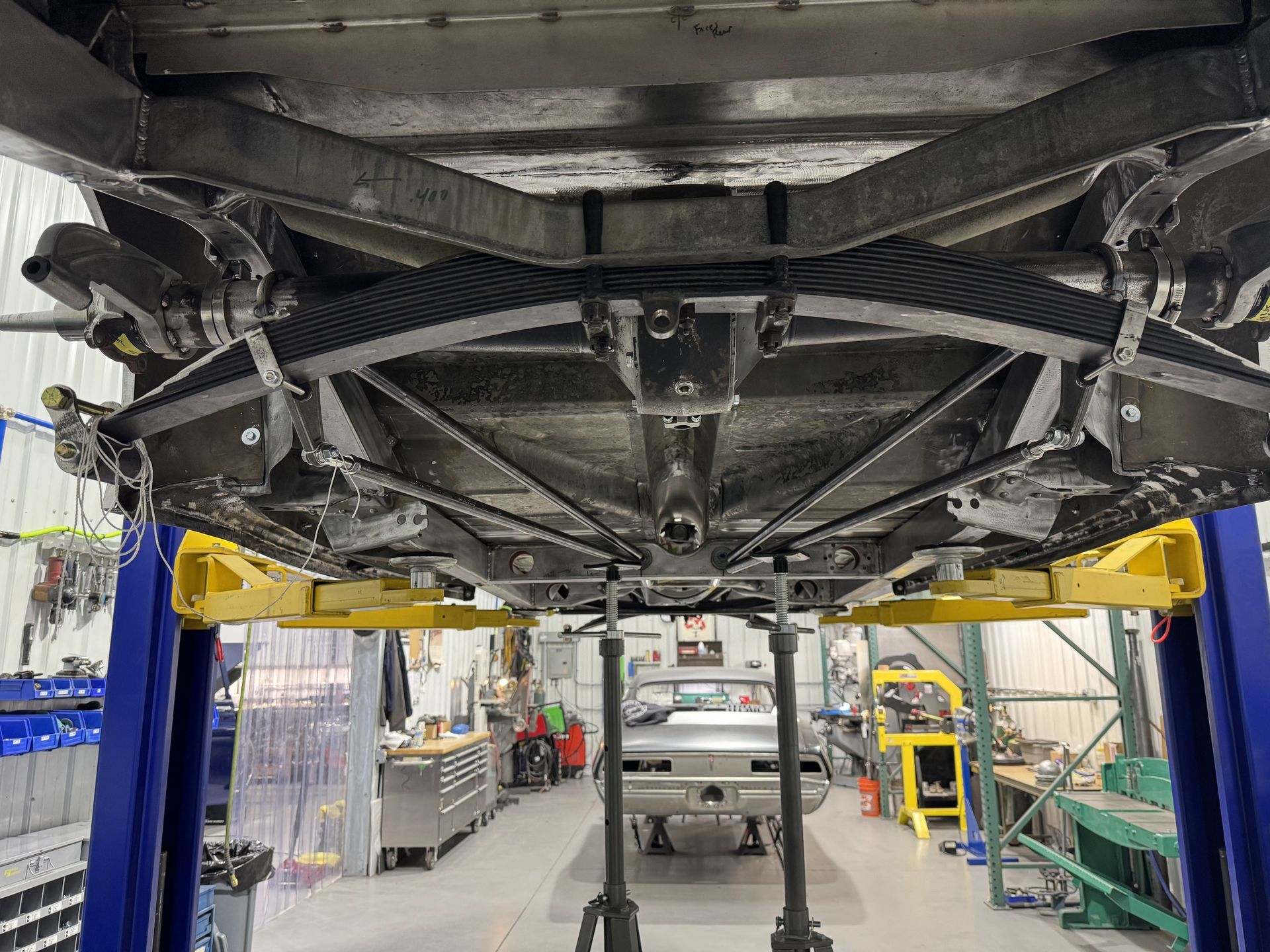 Undercarriage of a car on a lift in an auto repair shop, showing suspension and exhaust components.