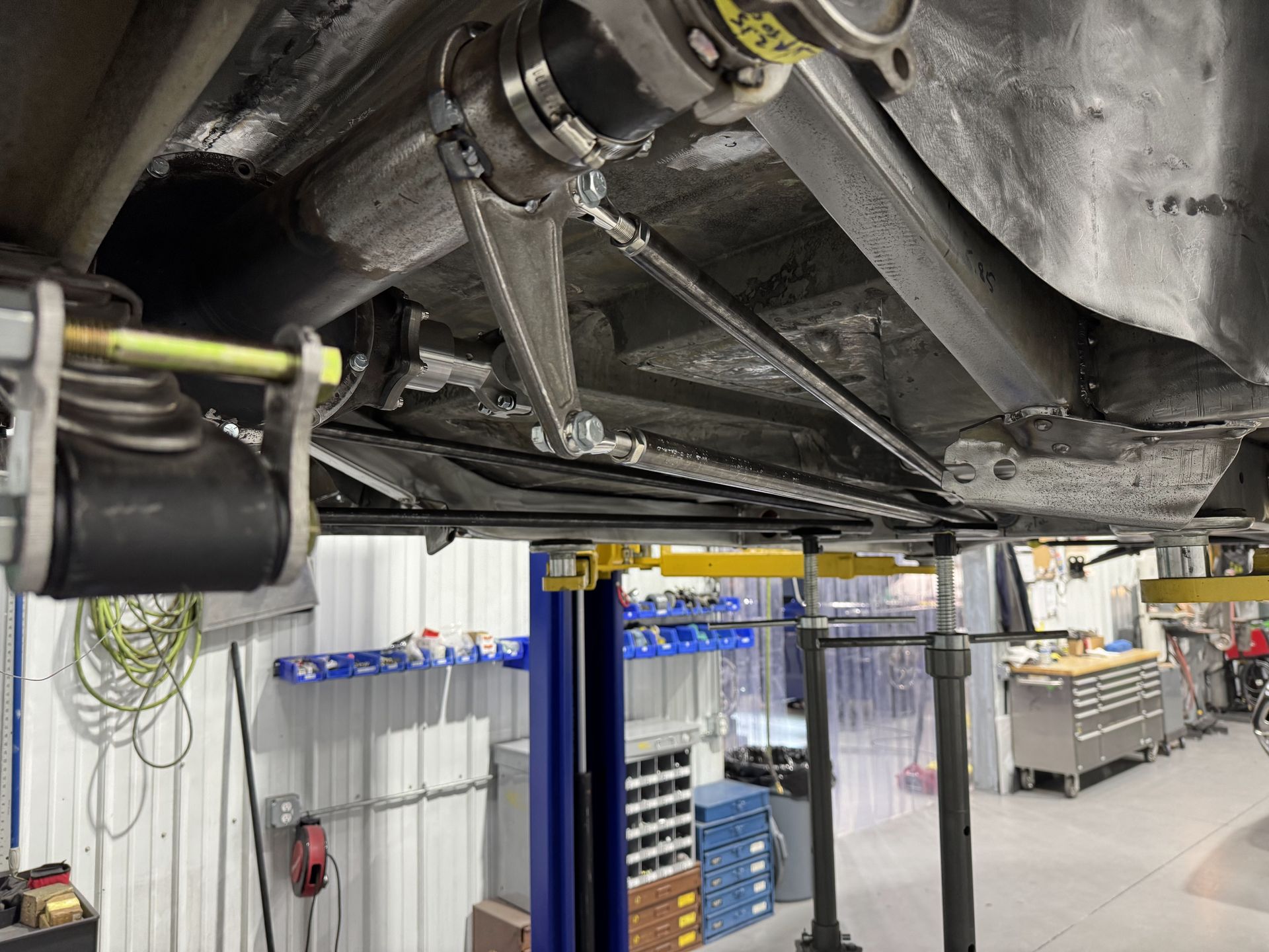 Underside of a vehicle on a lift in an auto repair shop, with tools and equipment in the background.
