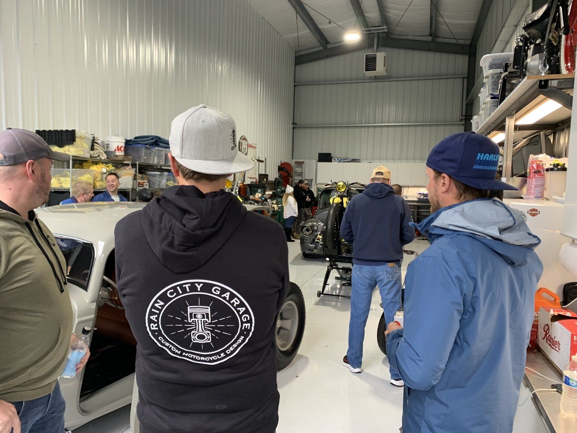People standing inside a warehouse workshop, facing a car and shelves of supplies.