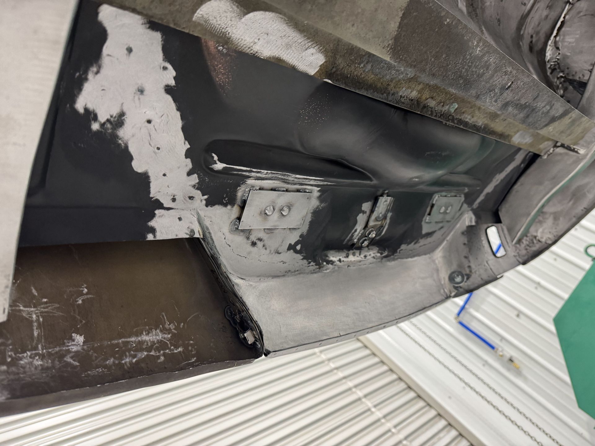 Close-up of a damaged black surface with chipped white paint and a patch in a workshop or garage.
