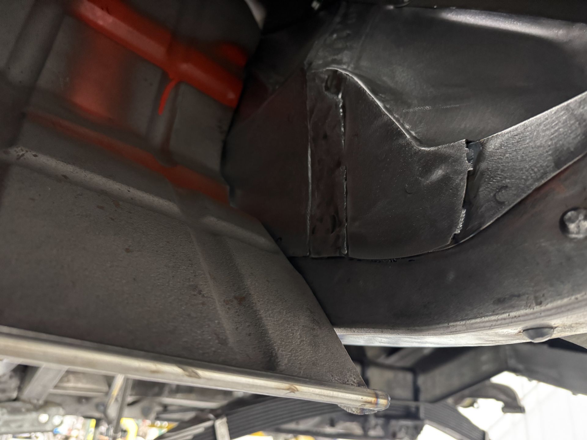 Underbody view of a vehicle with black metal panels, red pipes, and exposed mechanical components