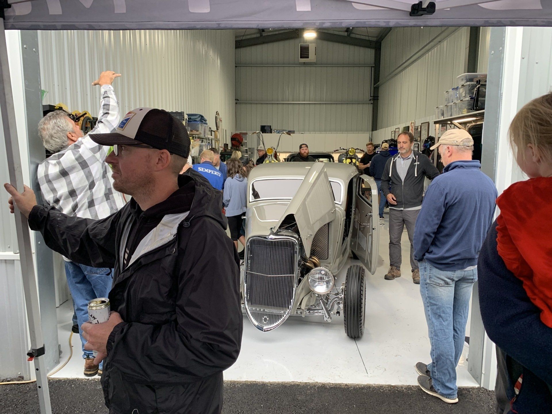 Classic car in a garage with people gathered around, front grille centered in the scene.