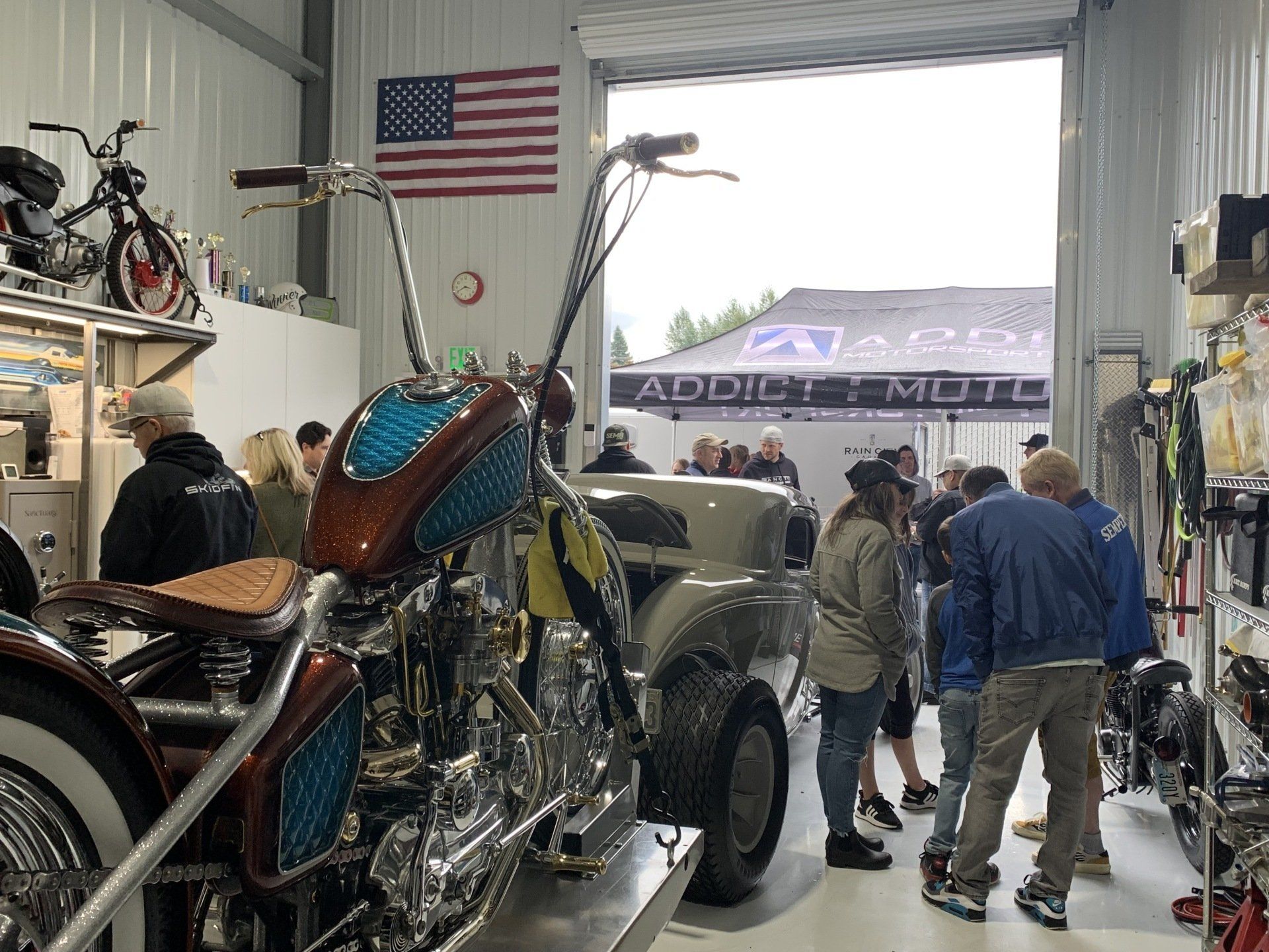Custom motorcycle inside a workshop with people gathered around and an American flag on the wall
