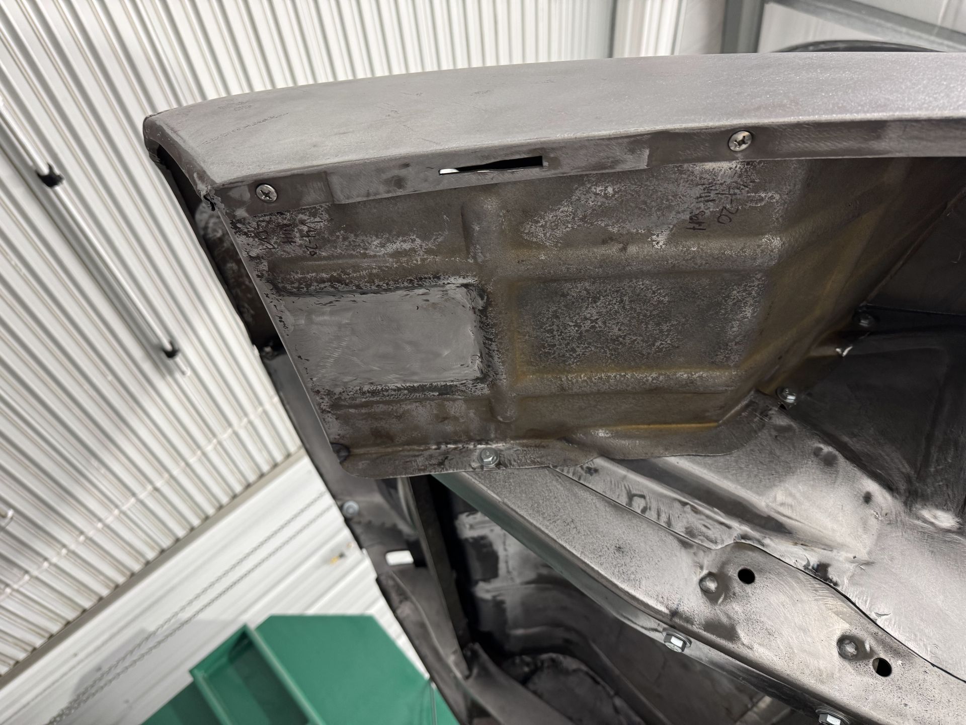 Close-up of a damaged car hood underside and inner panel in a garage-like setting