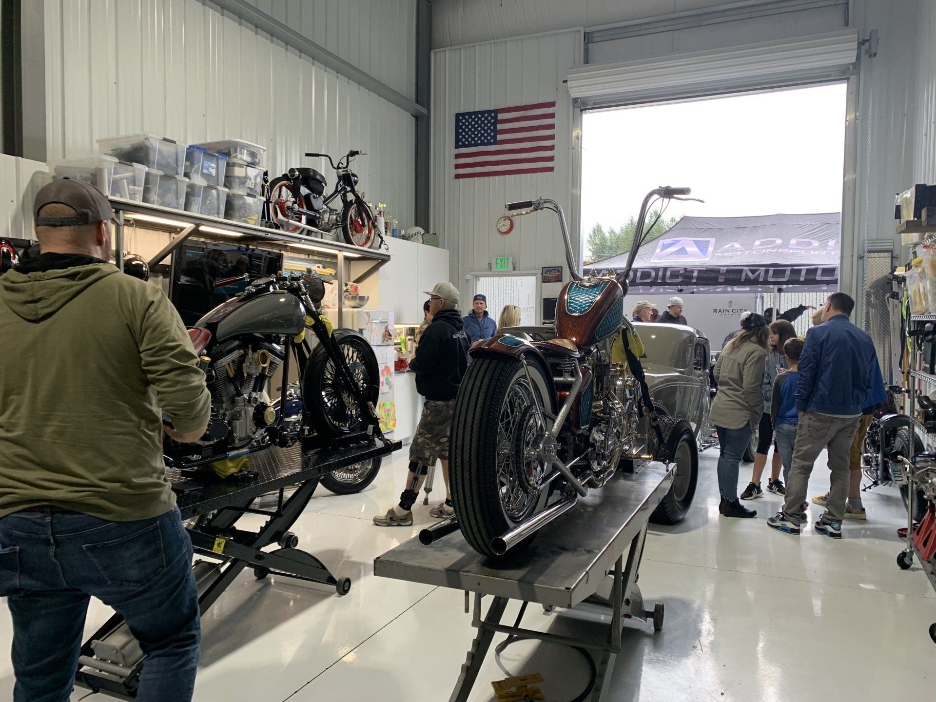 Motorcycles being assembled in a workshop, with several people working near an open garage door.
