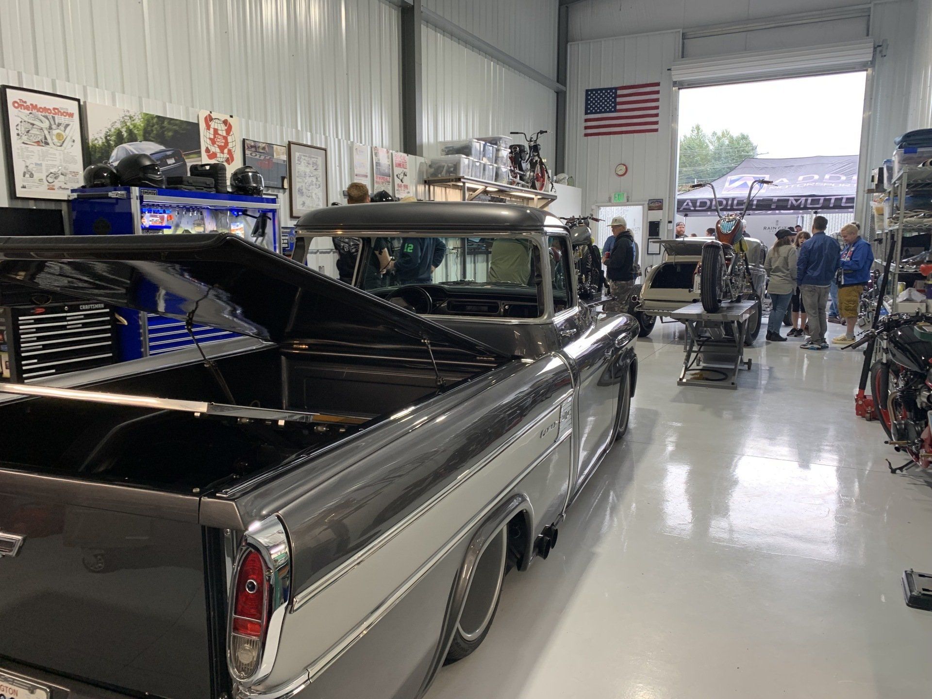 Classic black pickup truck inside a garage with people and equipment in the background