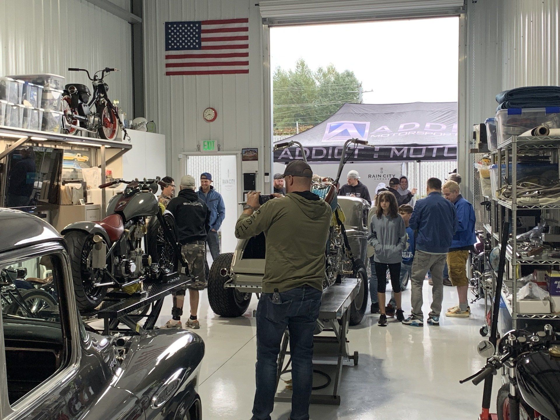 Group of people gathered in a motorcycle showroom, with bikes on display and an American flag on the wall