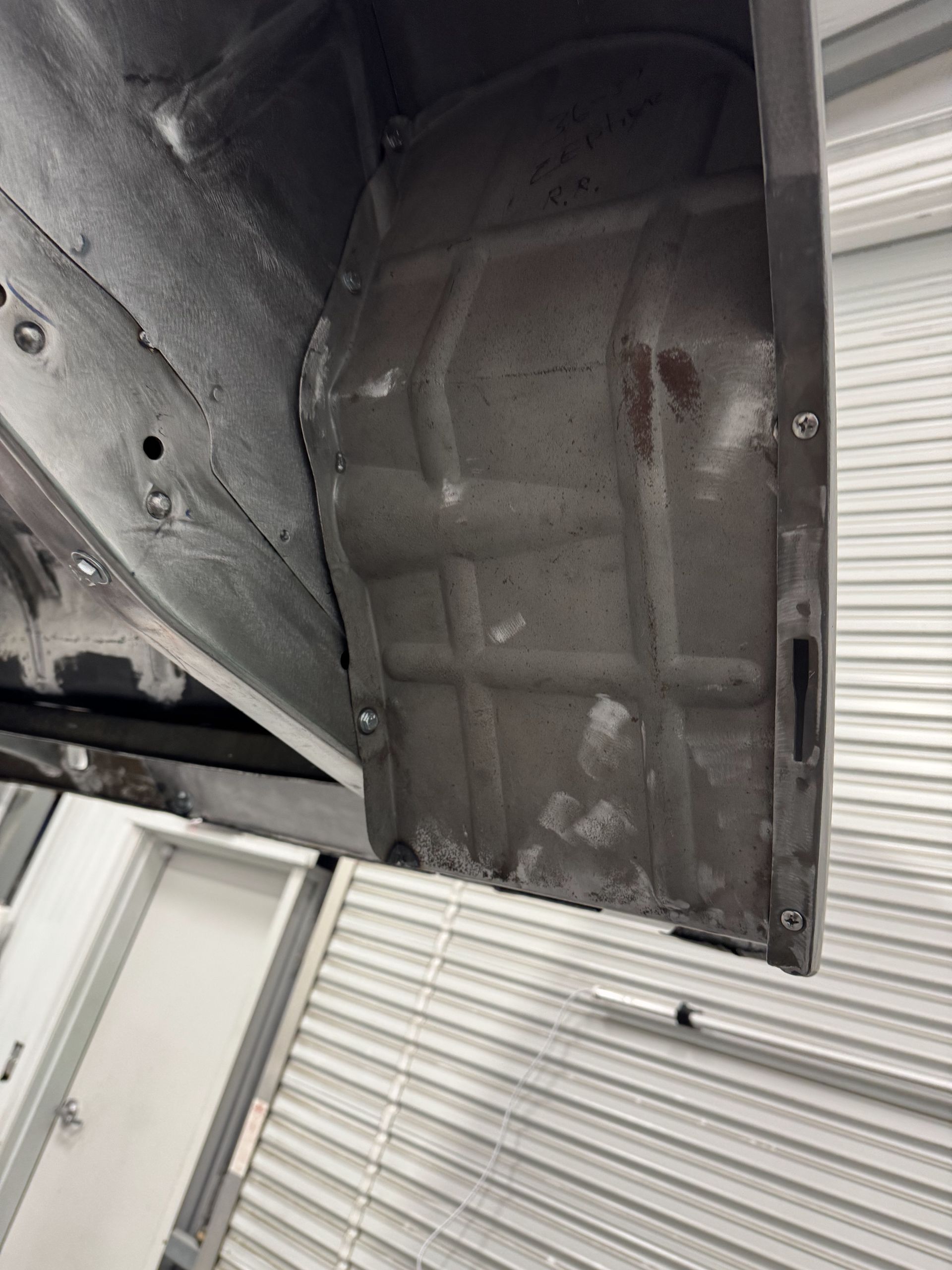 Undercarriage of a vehicle showing a dark wheel well and metal body panel against a corrugated garage door background