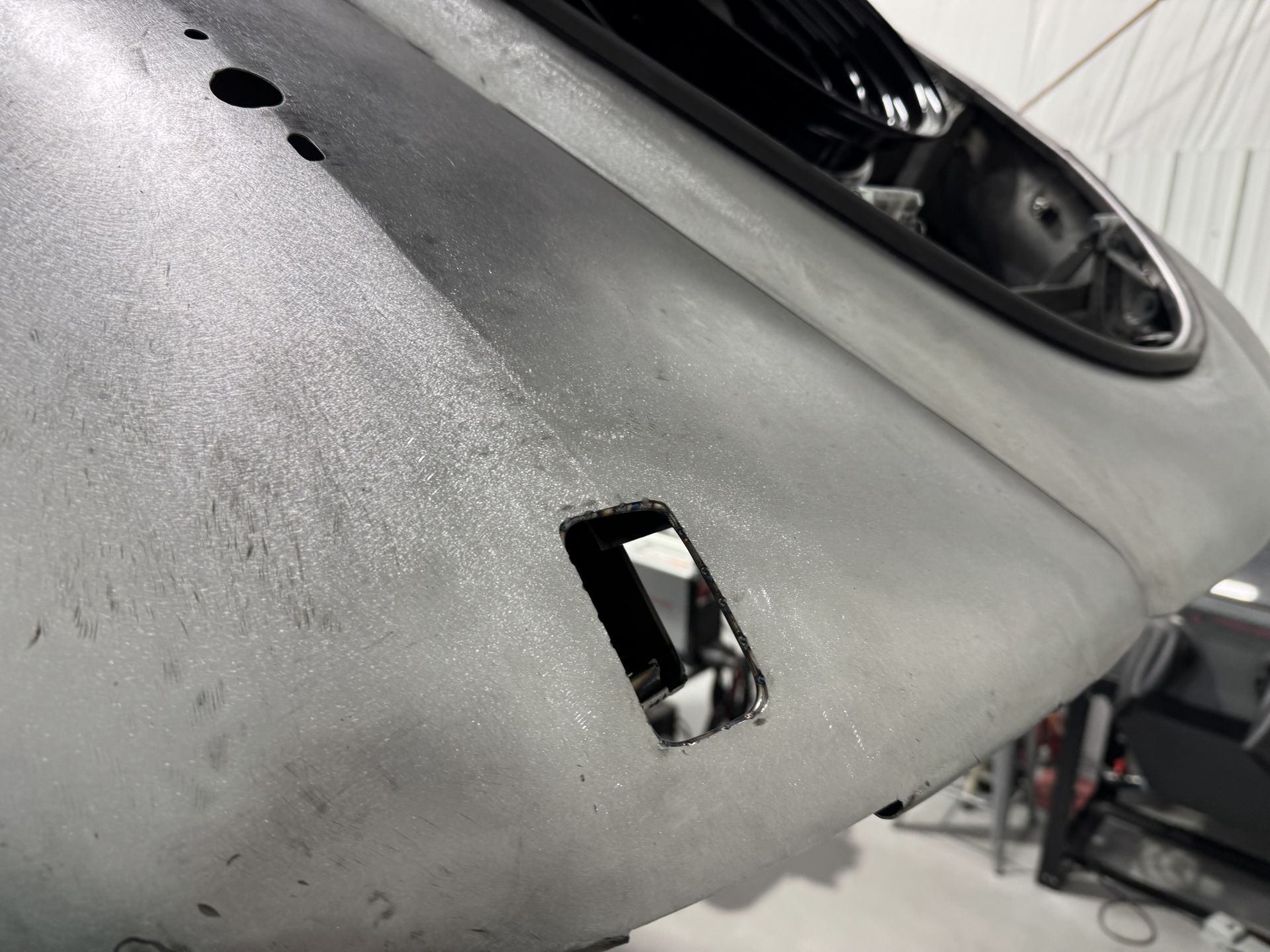 Damaged silver car bumper with a small rectangular opening and visible internal parts