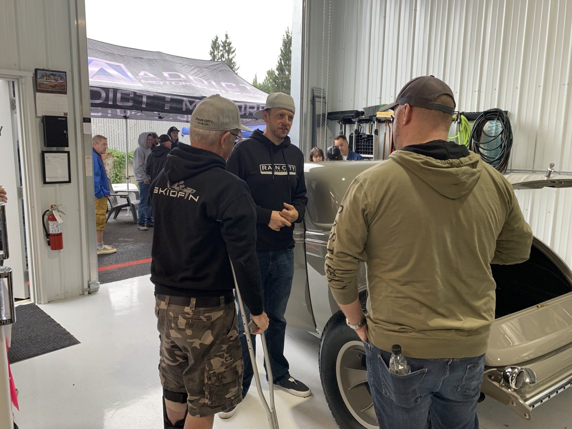 Three people talking beside a classic car inside a garage-like showroom