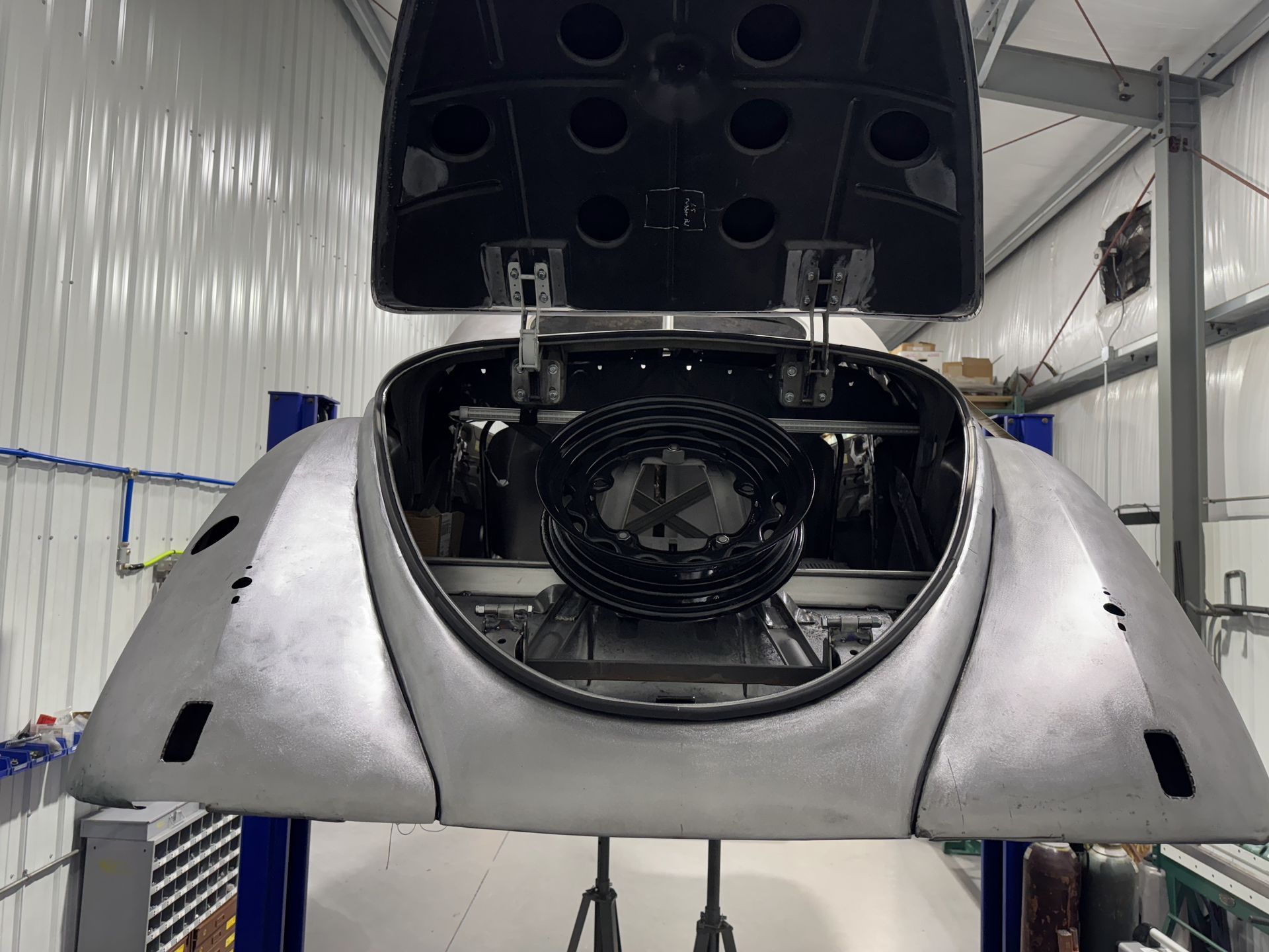 Silver sports car with rear hatch open, showing a large fan in a garage-like workshop.