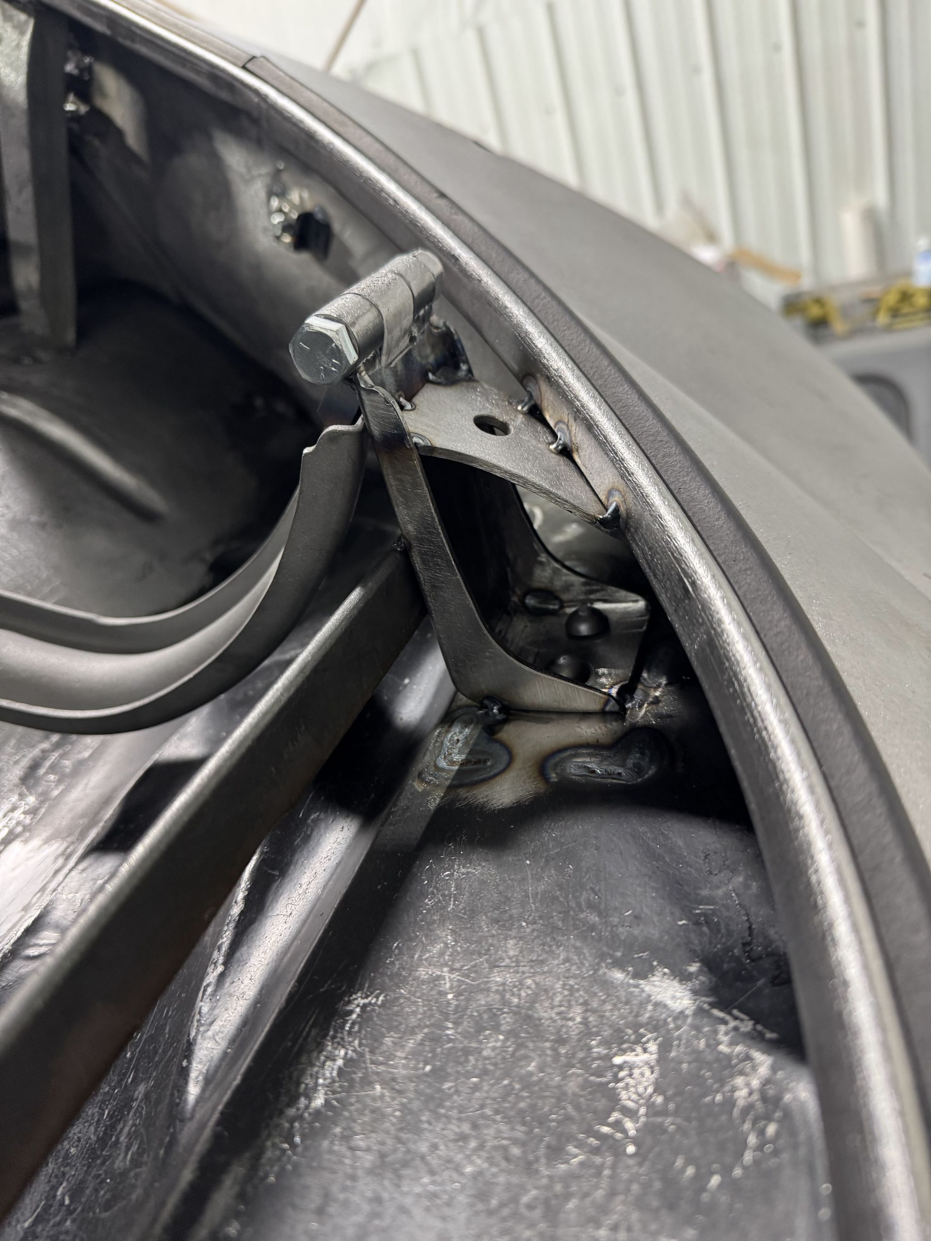 Close-up of a damaged black car door hinge and weather stripping inside a vehicle frame
