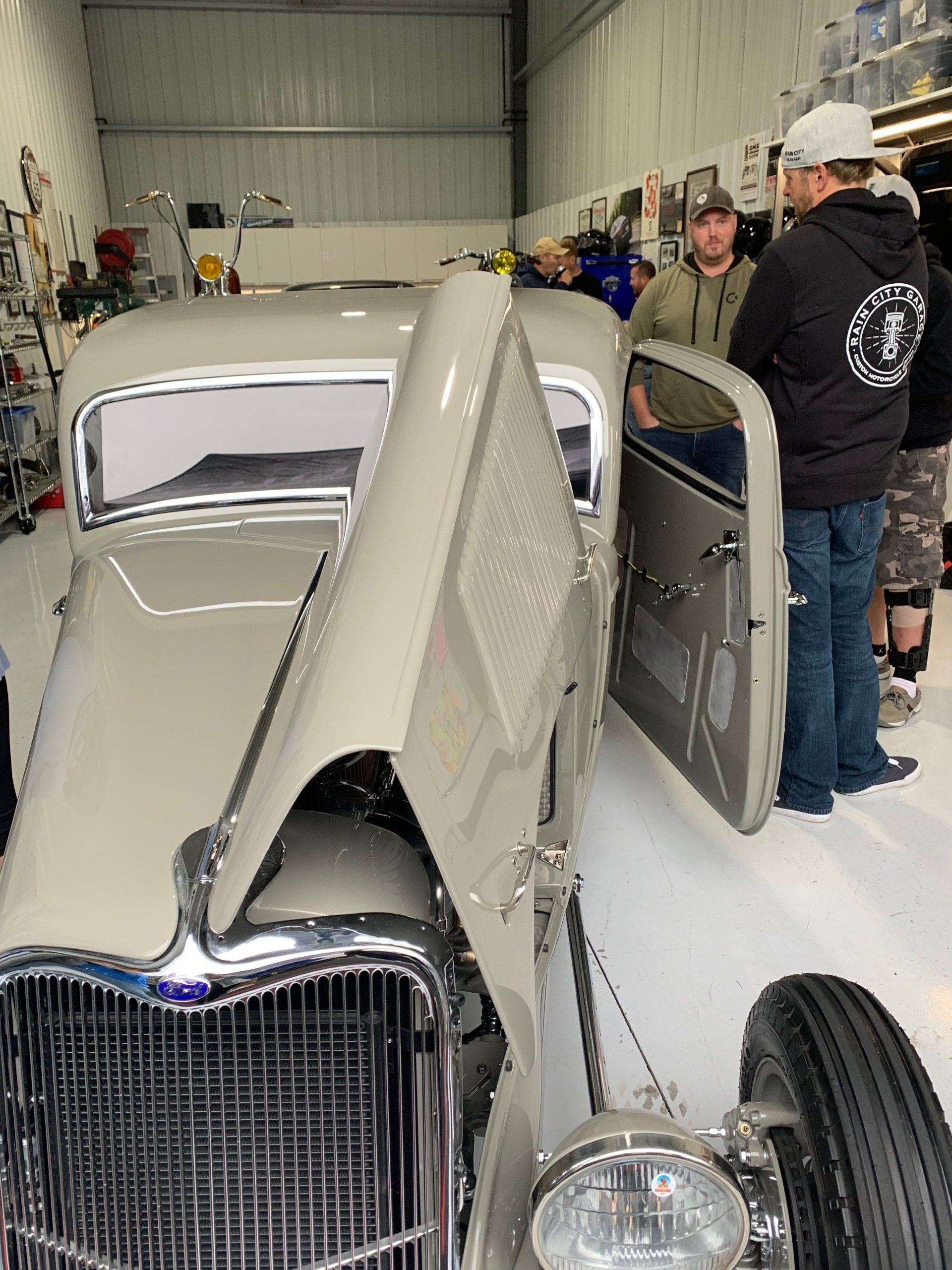 Two people beside a vintage white car with its hood open inside a garage