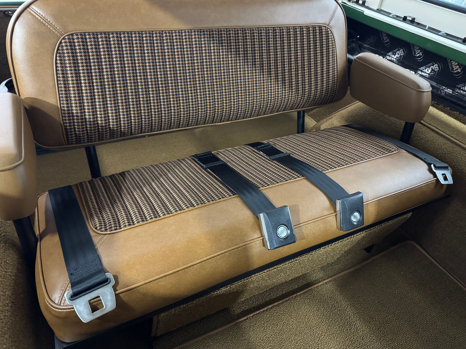 Tan upholstered car bench seat with brown patterned cushions and black seat belts.