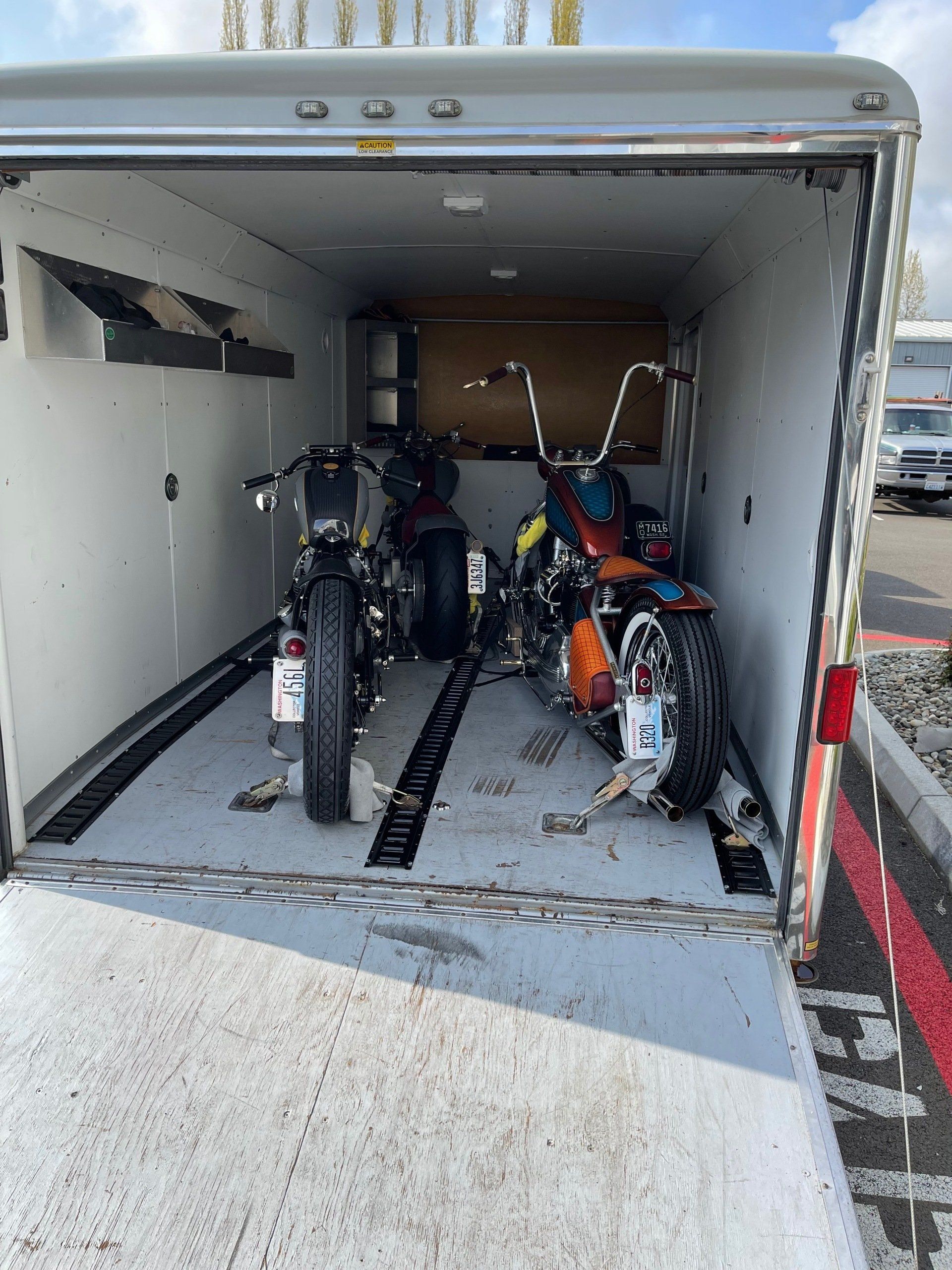 Open cargo trailer with several motorcycles secured inside, viewed from the rear ramp.