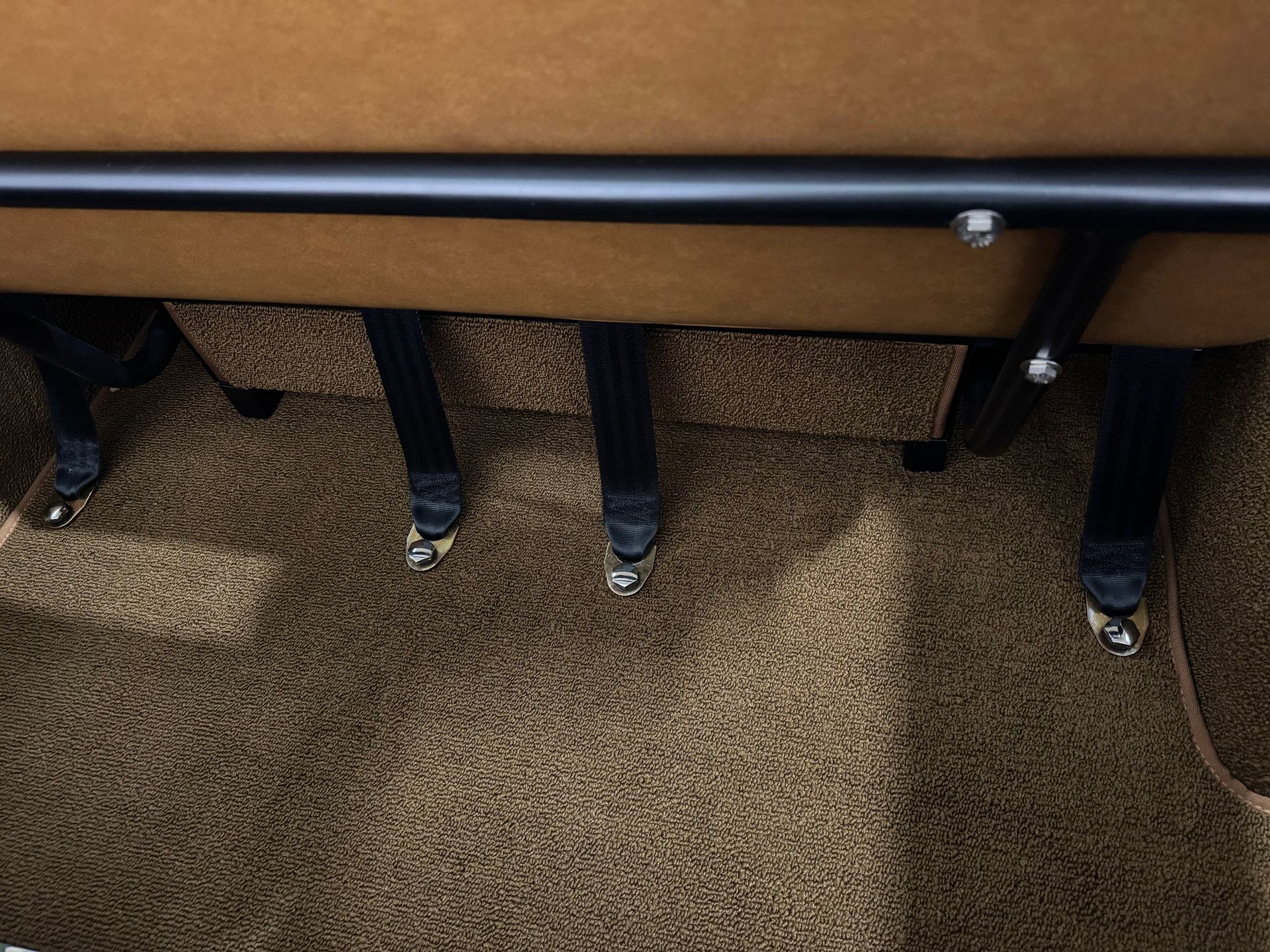 Under-desk view with several legs and black shoes on tan carpet beneath a table or bench