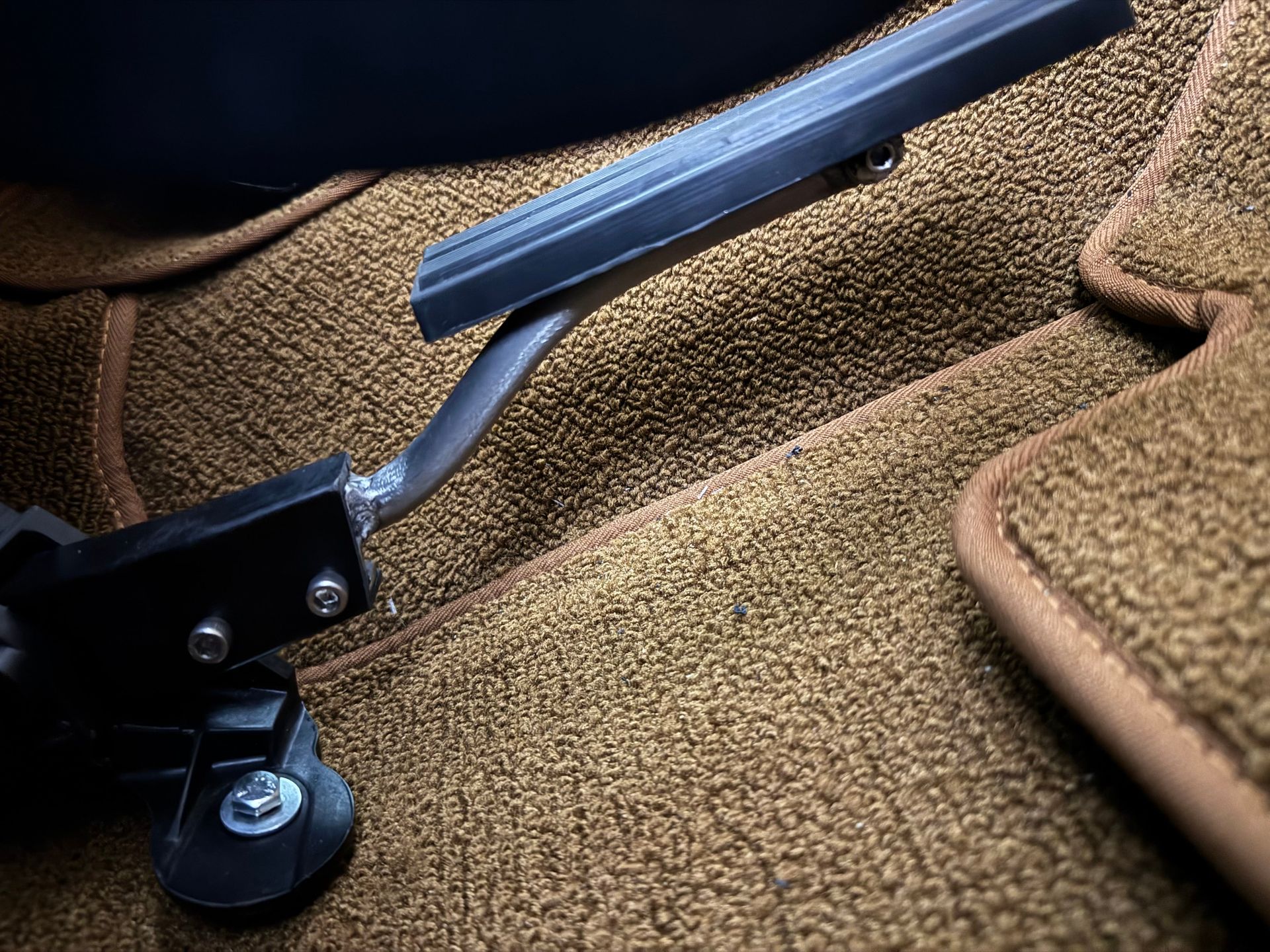 Close-up of a car seat adjustment lever on tan upholstery with black and silver hardware