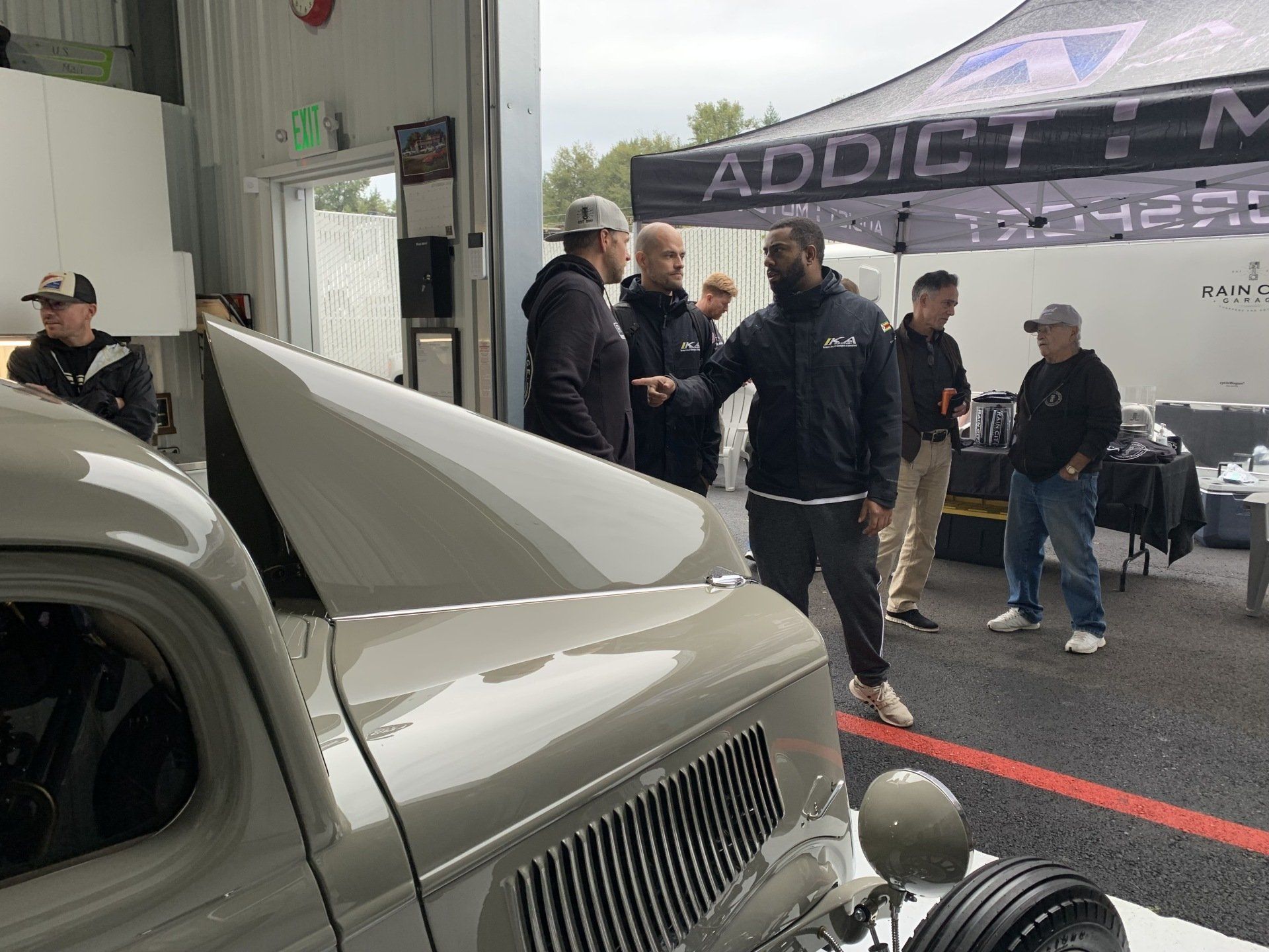 Group of people standing beside a white classic car under a tent at an outdoor event