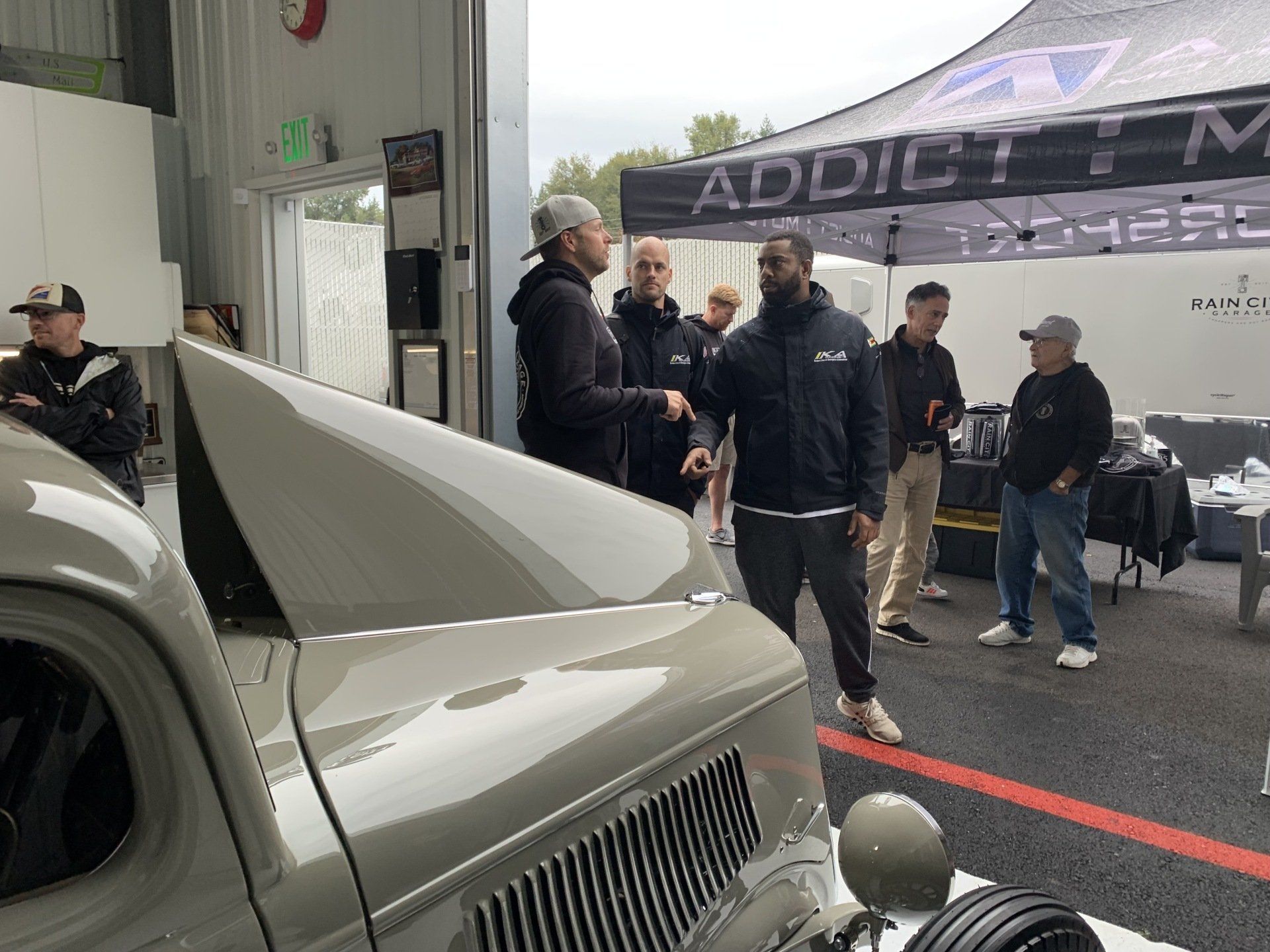 Classic car under a tent at an indoor auto show, with several people gathered around it.