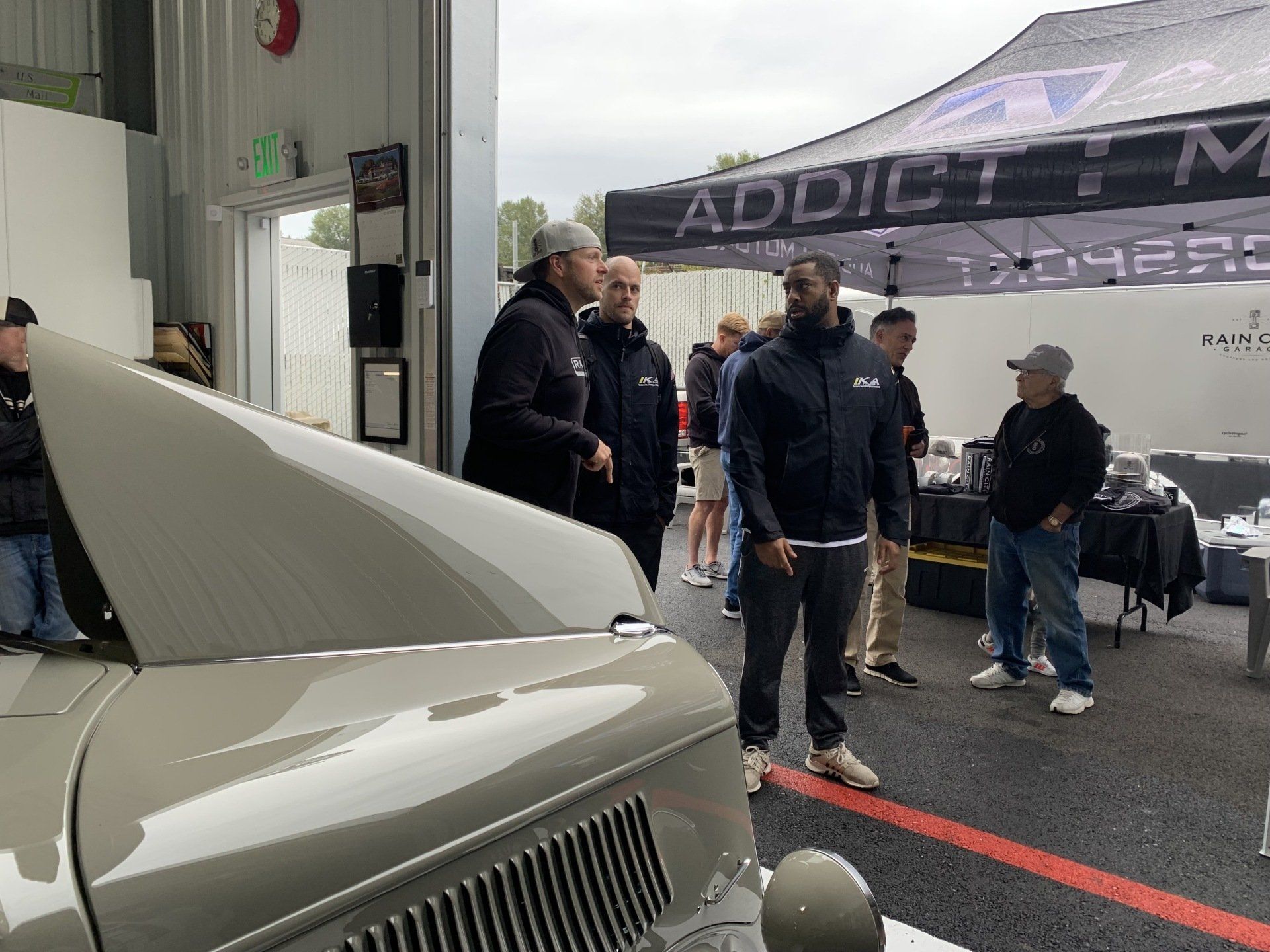 Classic car in a garage with people standing nearby under an ADDICTM tent.