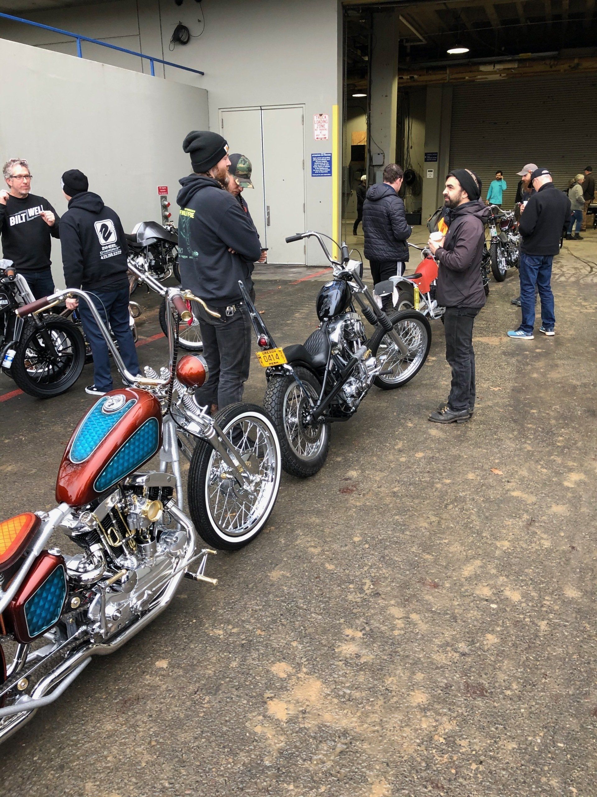 Motorcycles lined up outside a building with a few people standing and talking nearby