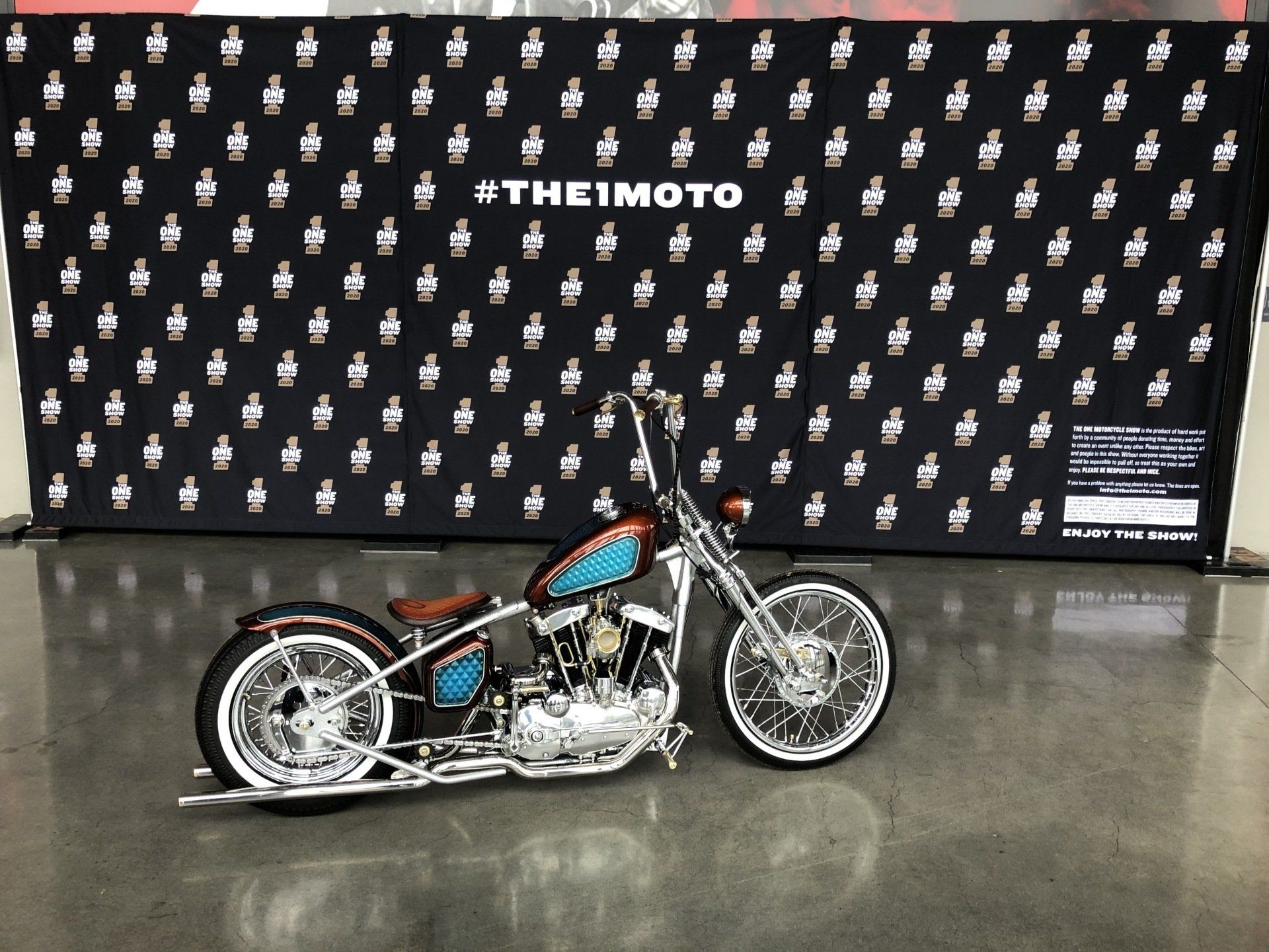 Custom chopper motorcycle on polished floor in front of a black #THETIMOTO backdrop