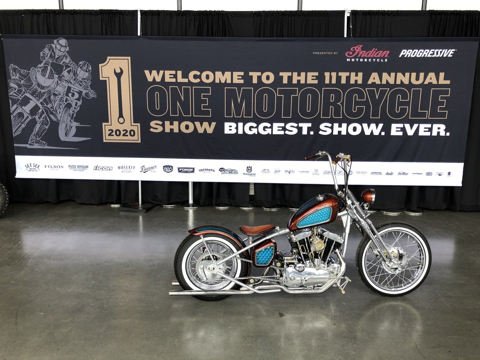 Custom motorcycle displayed in front of a large “Welcome to the 11th Annual One Motorcycle Show” banner.