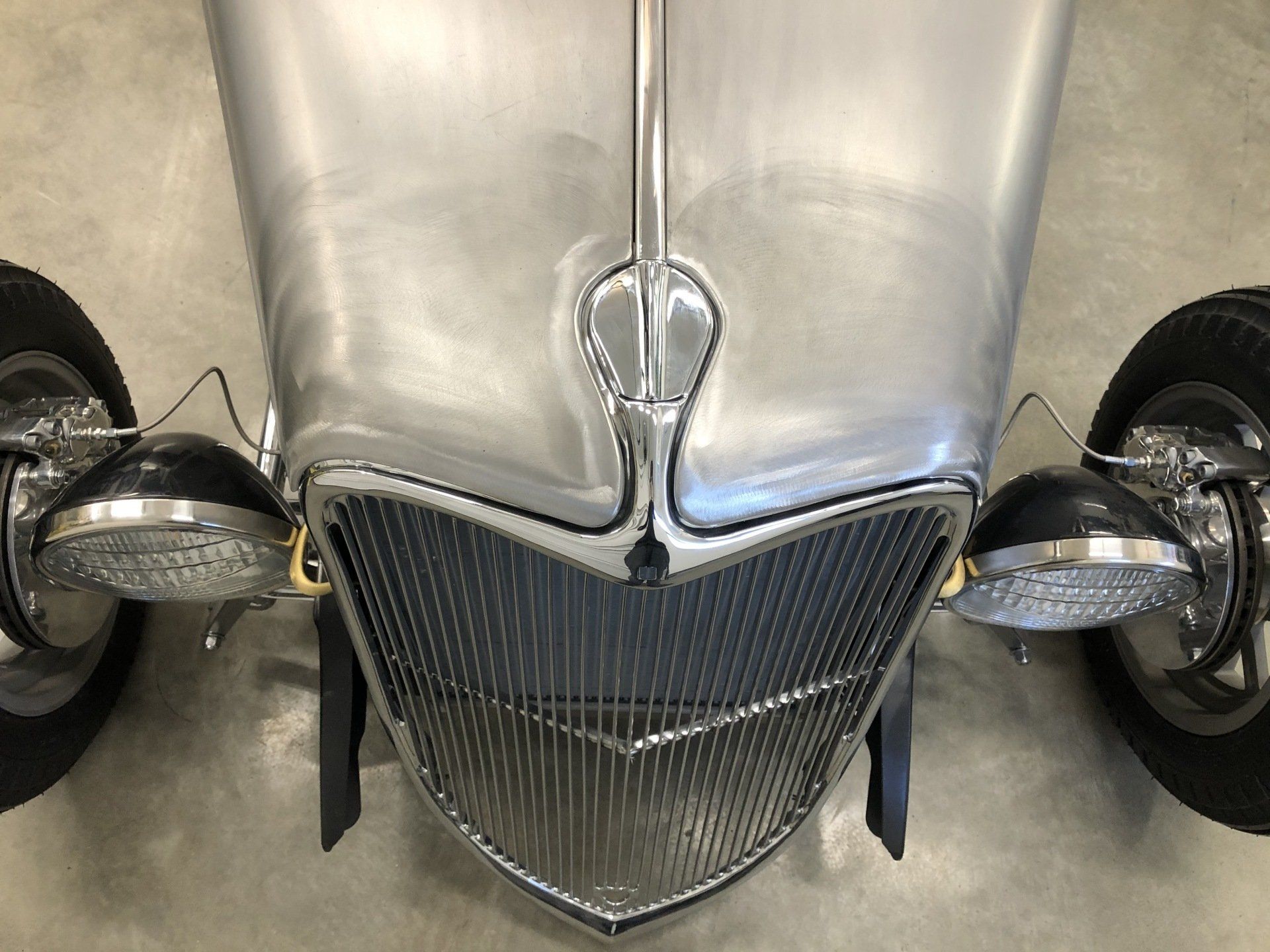 Front view of a silver vintage car with black wheels and chrome grille