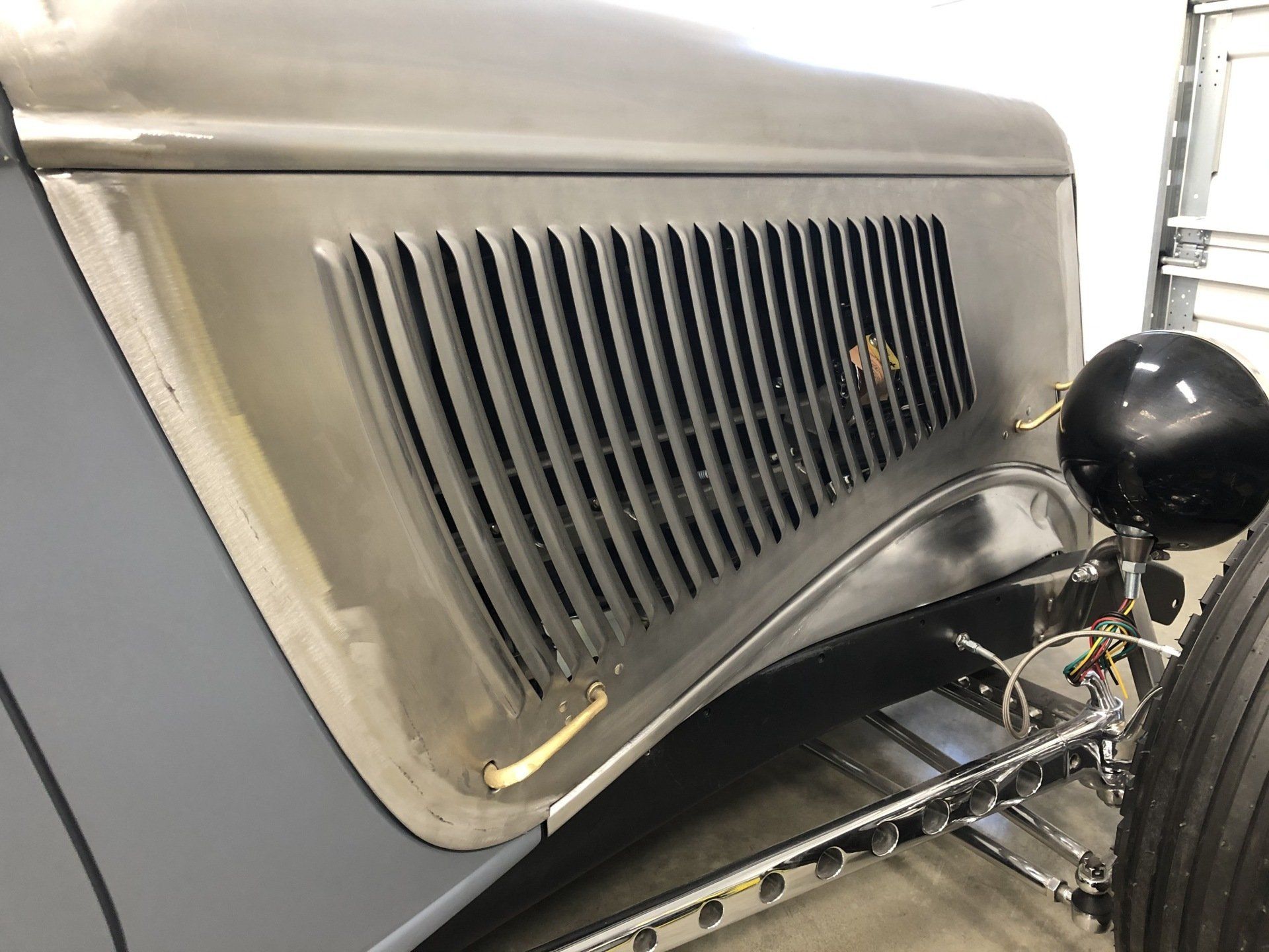Close-up of a vintage car’s front grille, hood, and headlight in a garage.
