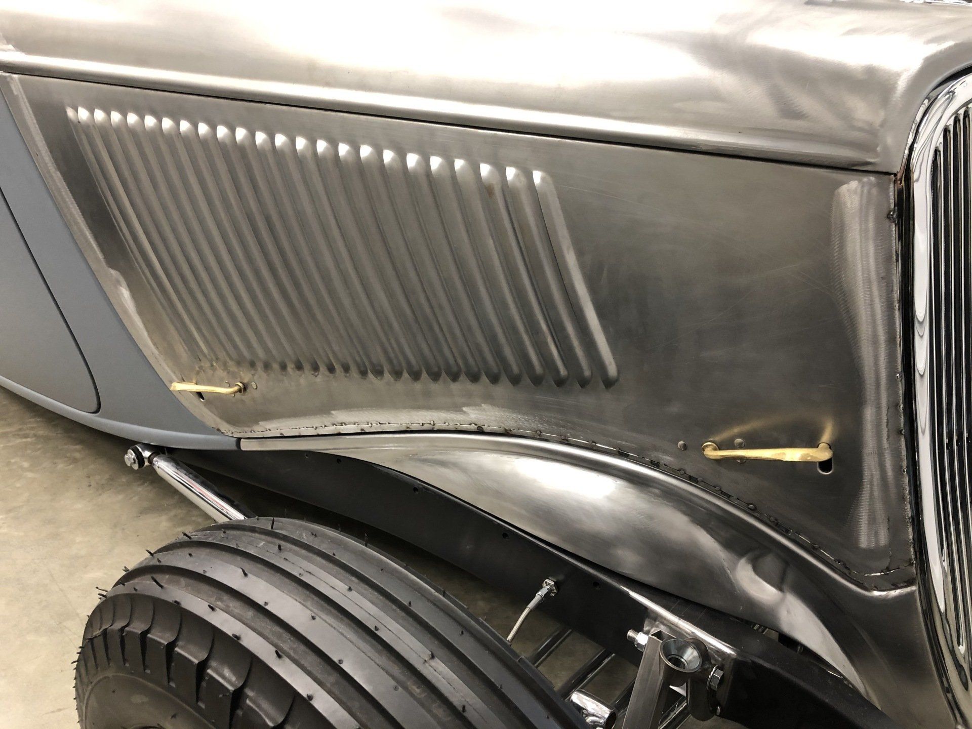 Close-up of a black vintage car’s rear quarter panel with a damaged wheel well and tire visible.