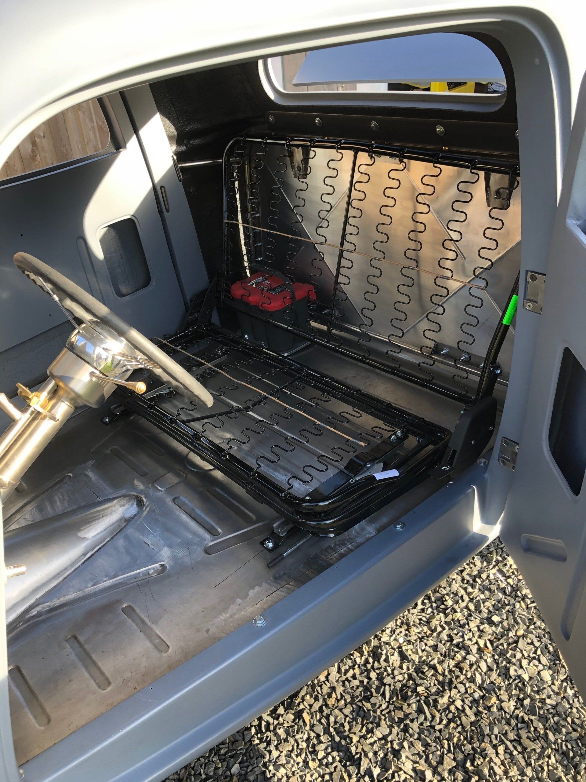 Car interior with stripped passenger seat area, exposed metal floor, and a brass tool resting inside.