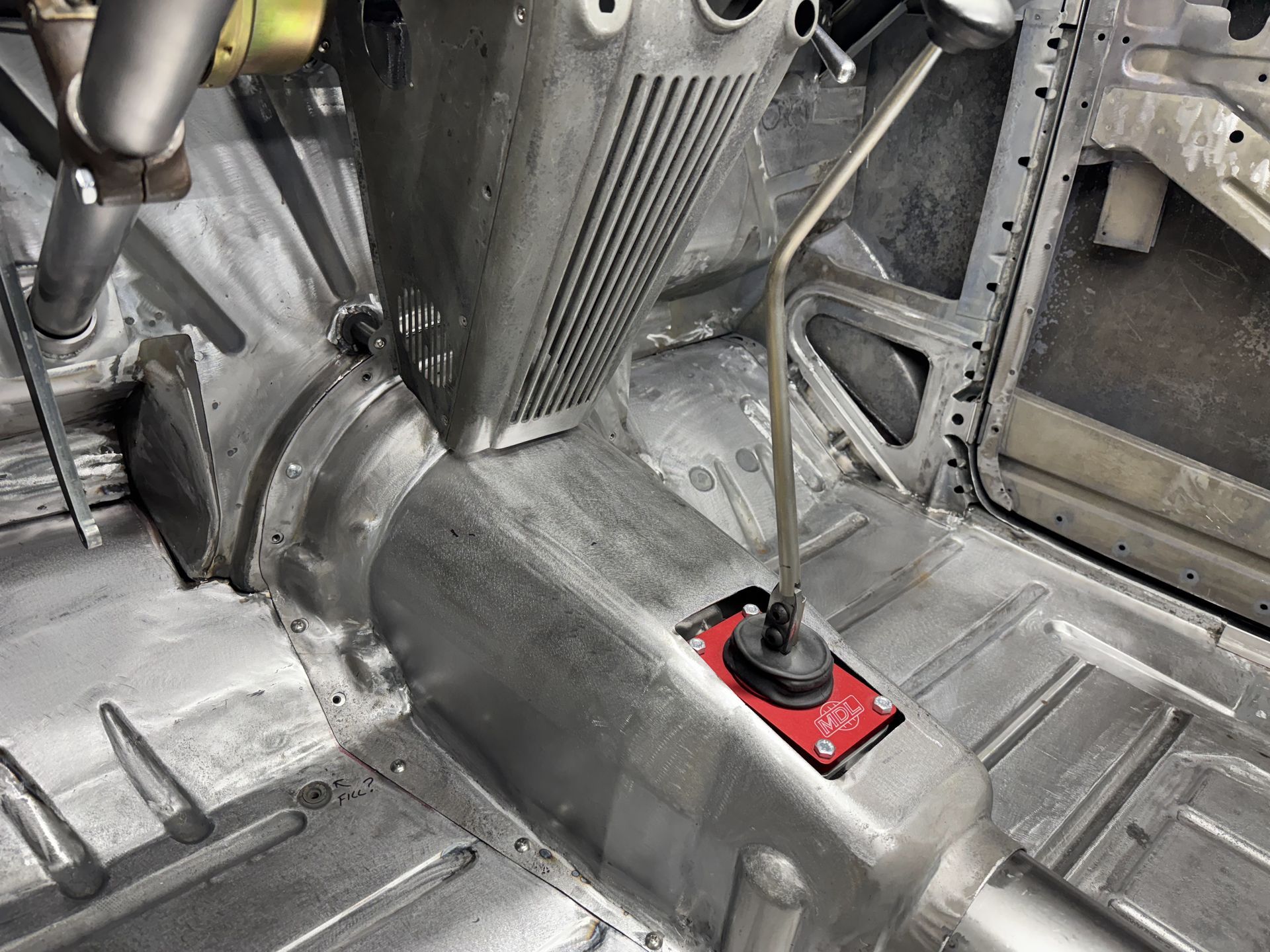 Inside a vintage car interior, a red toggle switch sits on the transmission tunnel near the seats.