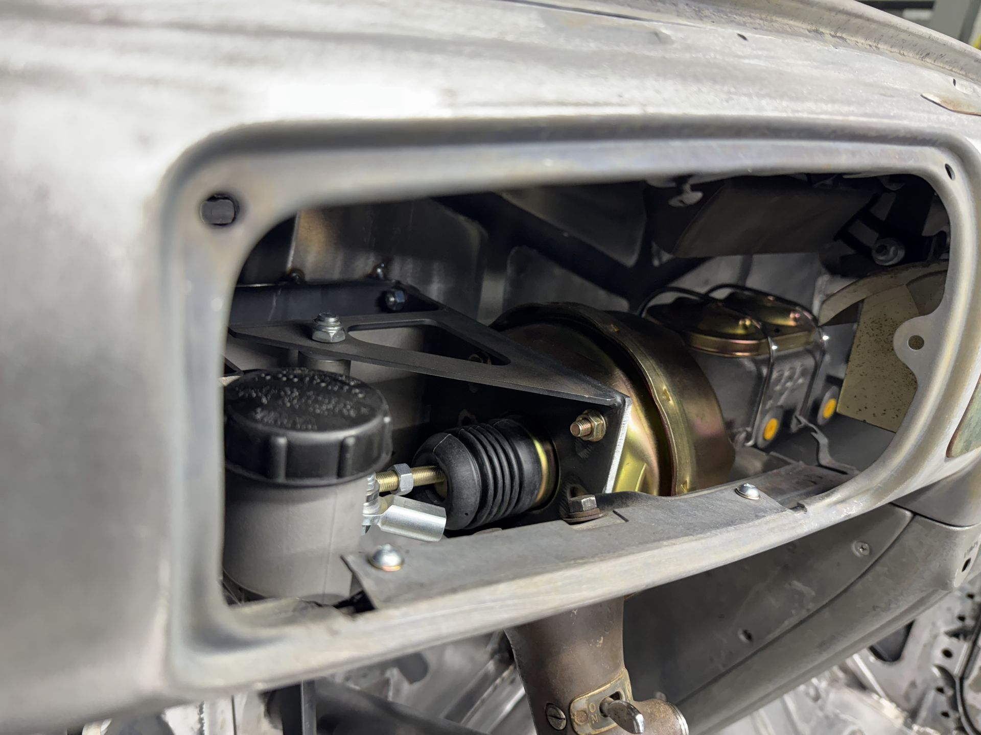 Close-up of a car engine compartment with exposed hoses and mechanical parts inside an open panel.