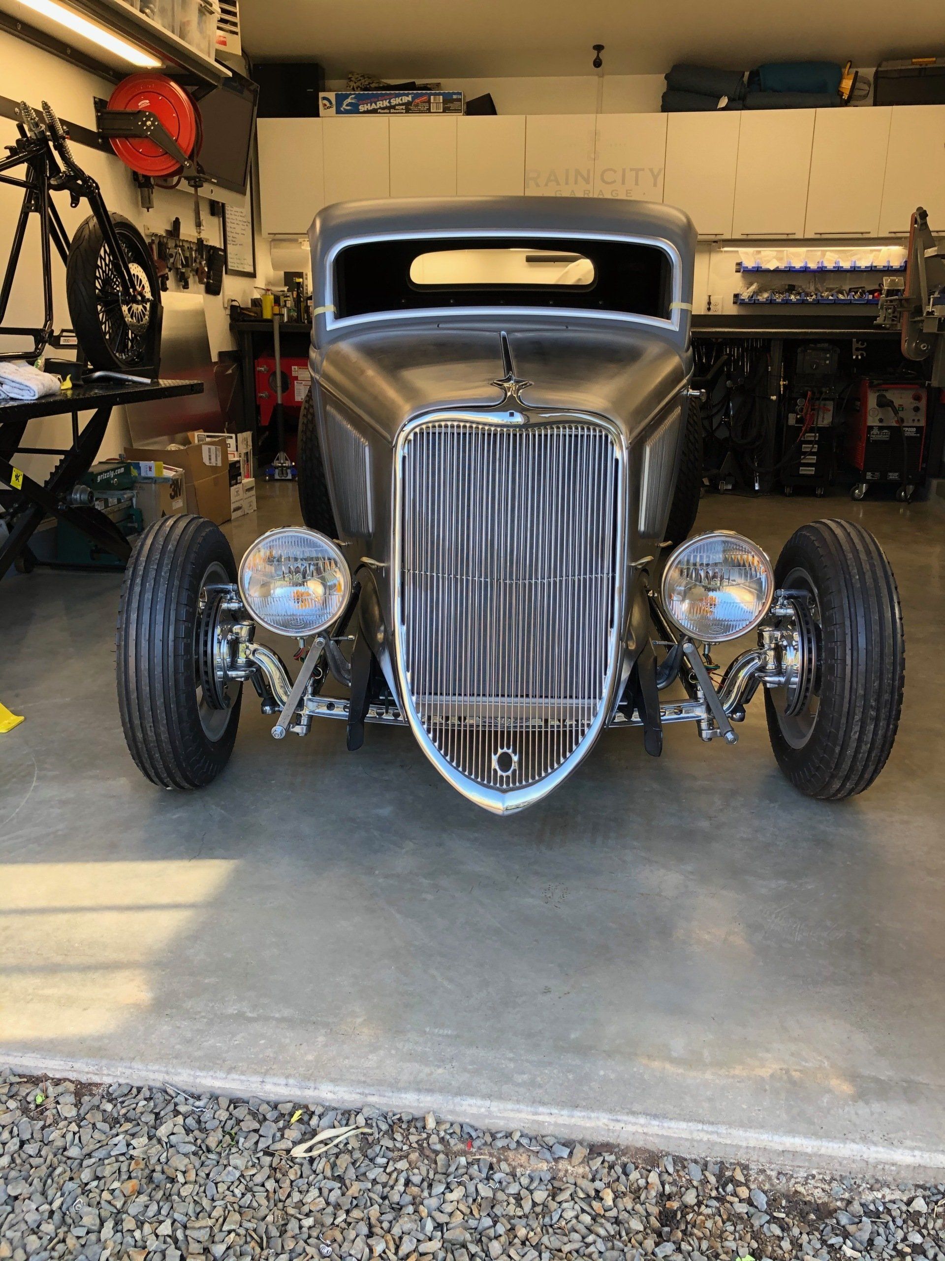 Vintage hot rod with chrome grille parked in a garage, front view on concrete floor.