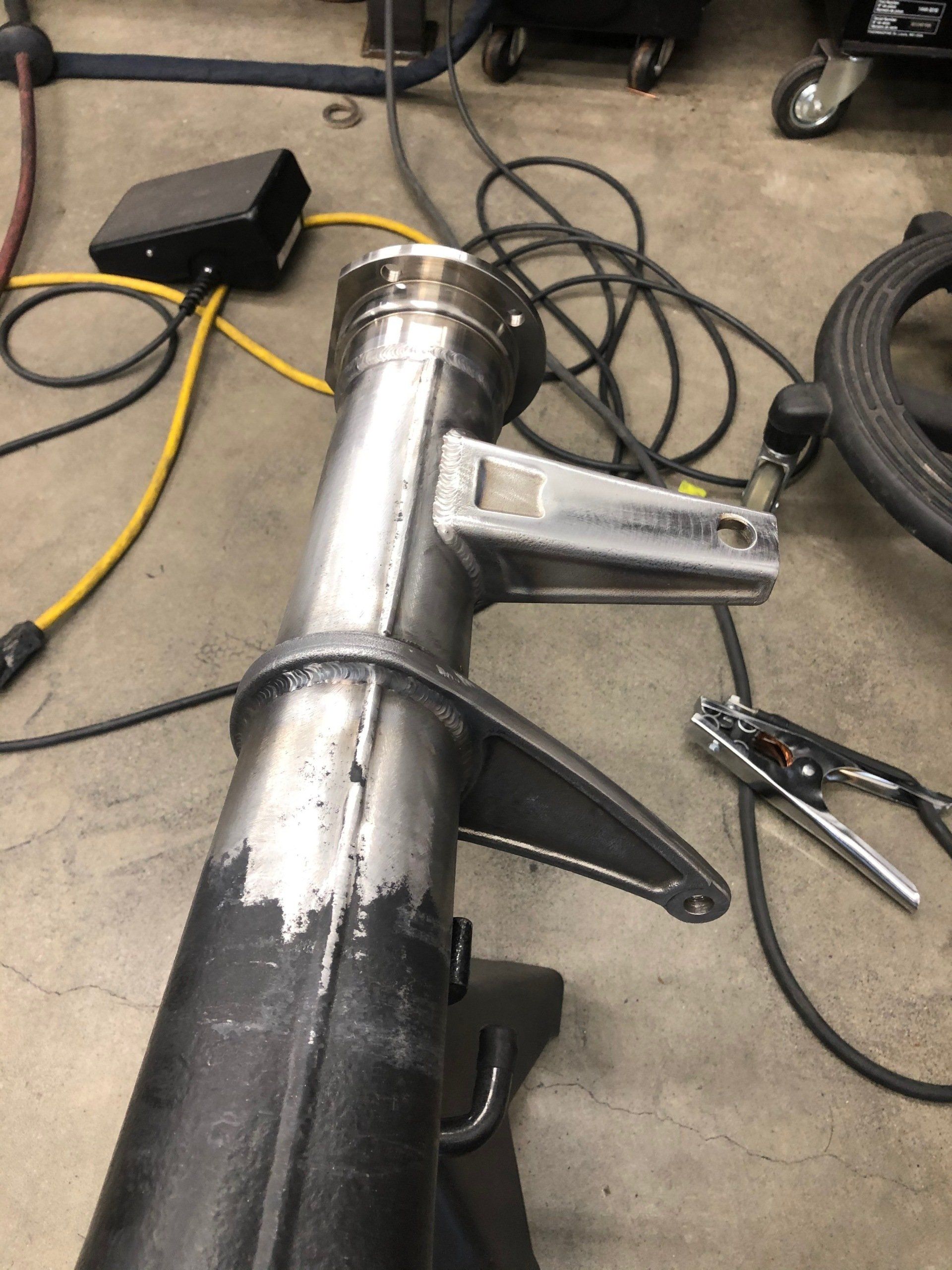 Workshop floor with a metal pipe assembly, cords, and hand tools scattered around.