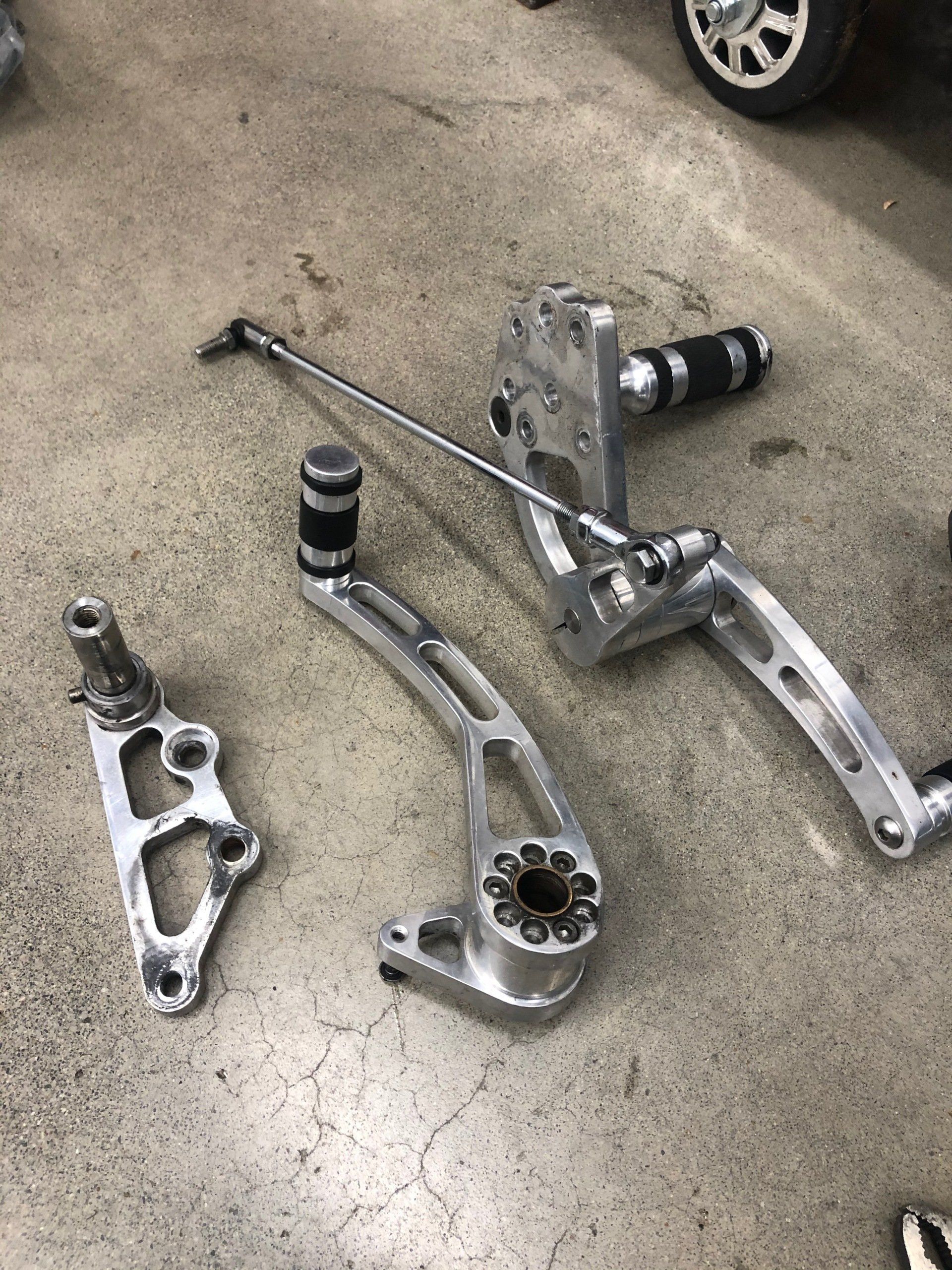 Scattered motorcycle foot pegs and levers on a concrete floor, with part of a vehicle wheel visible.