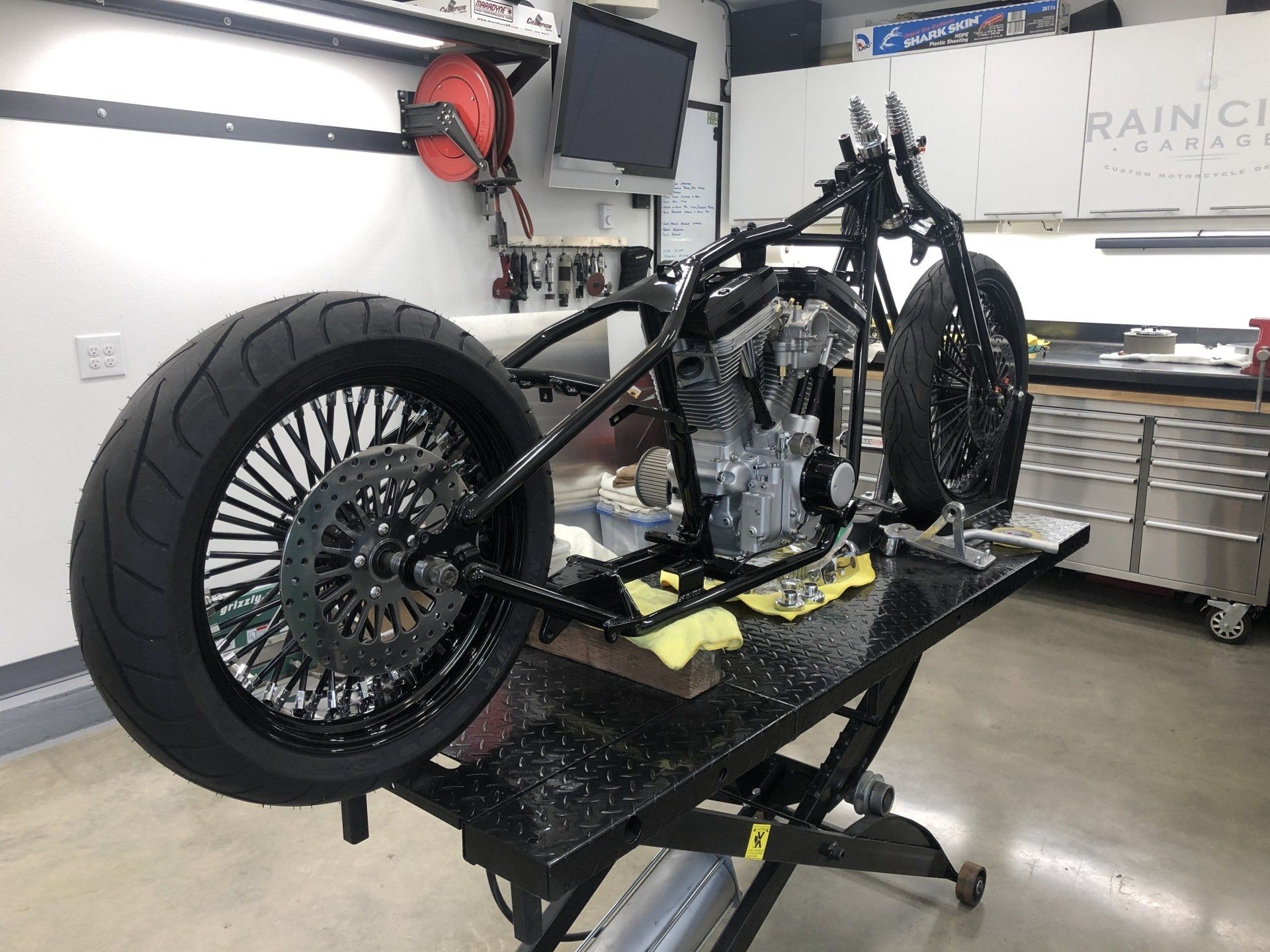 Custom motorcycle frame and rear wheel on a lift in a garage workshop