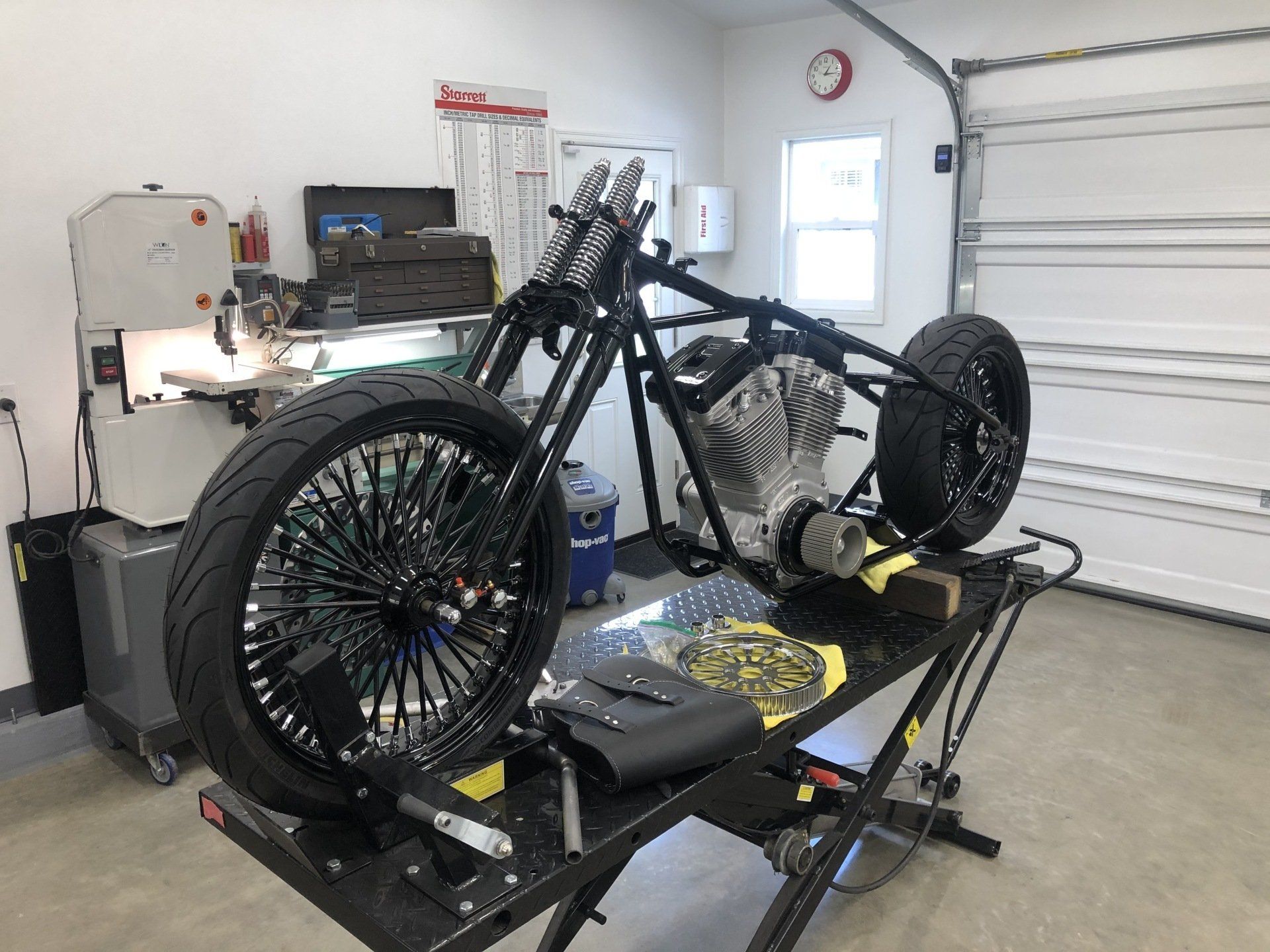 Black motorcycle on a lift in a garage, with a loose rear wheel and tools nearby