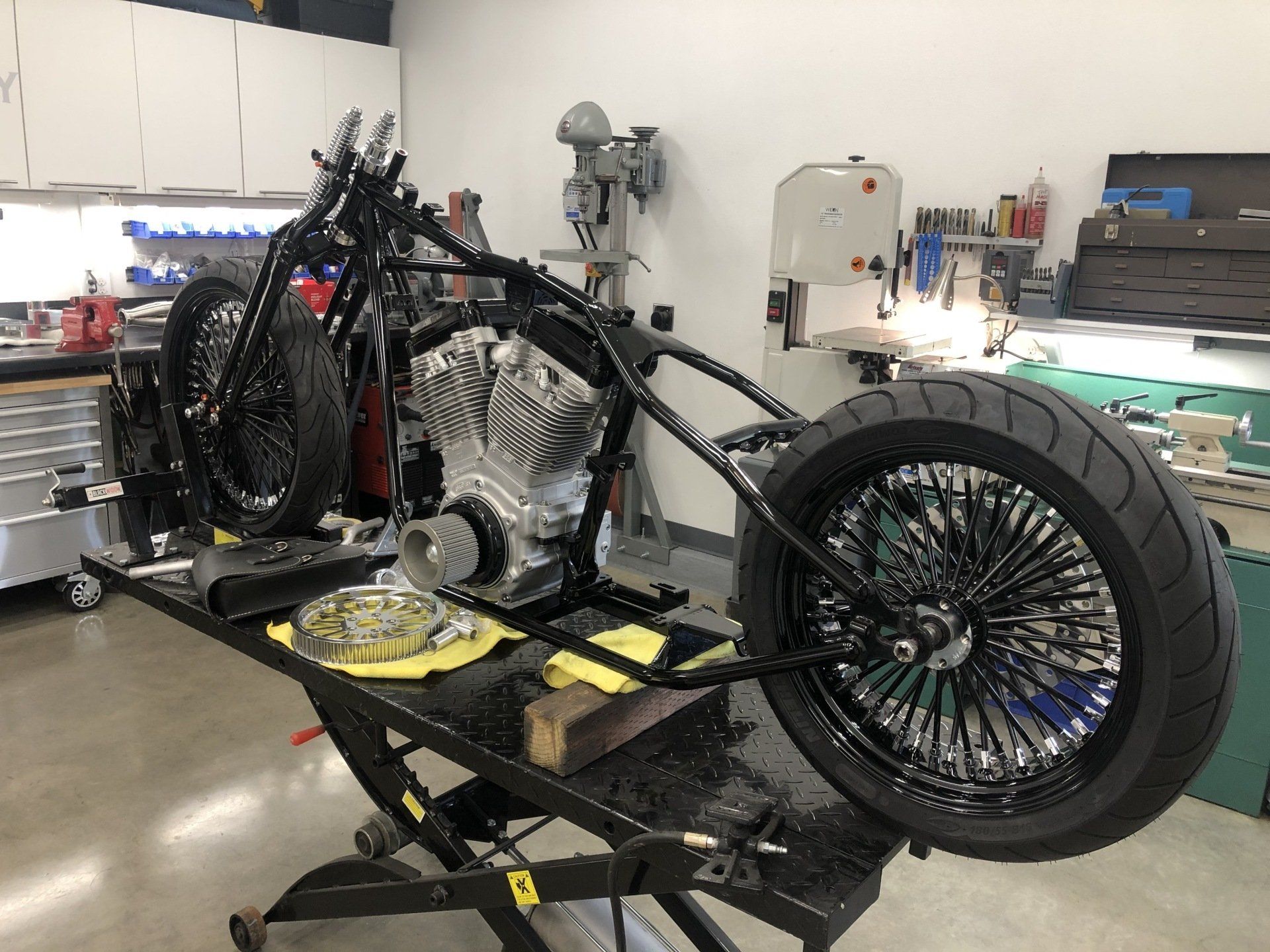 Custom motorcycle chassis in a workshop, with large rear wheel and exposed engine on a lift.