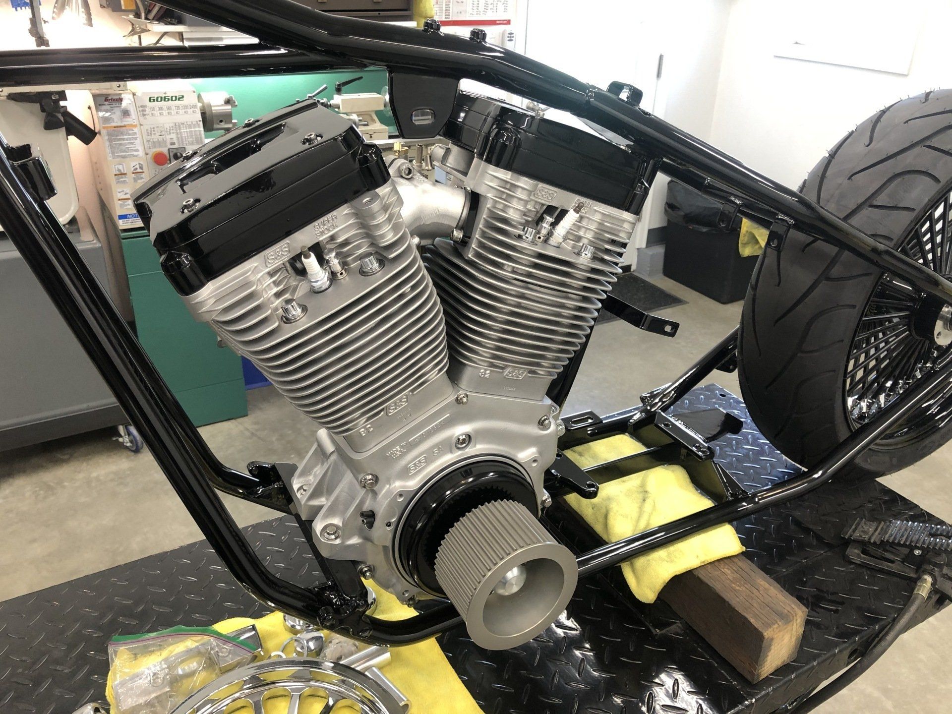 V-twin engine mounted in a custom bike frame, with a large rear tire in a workshop.