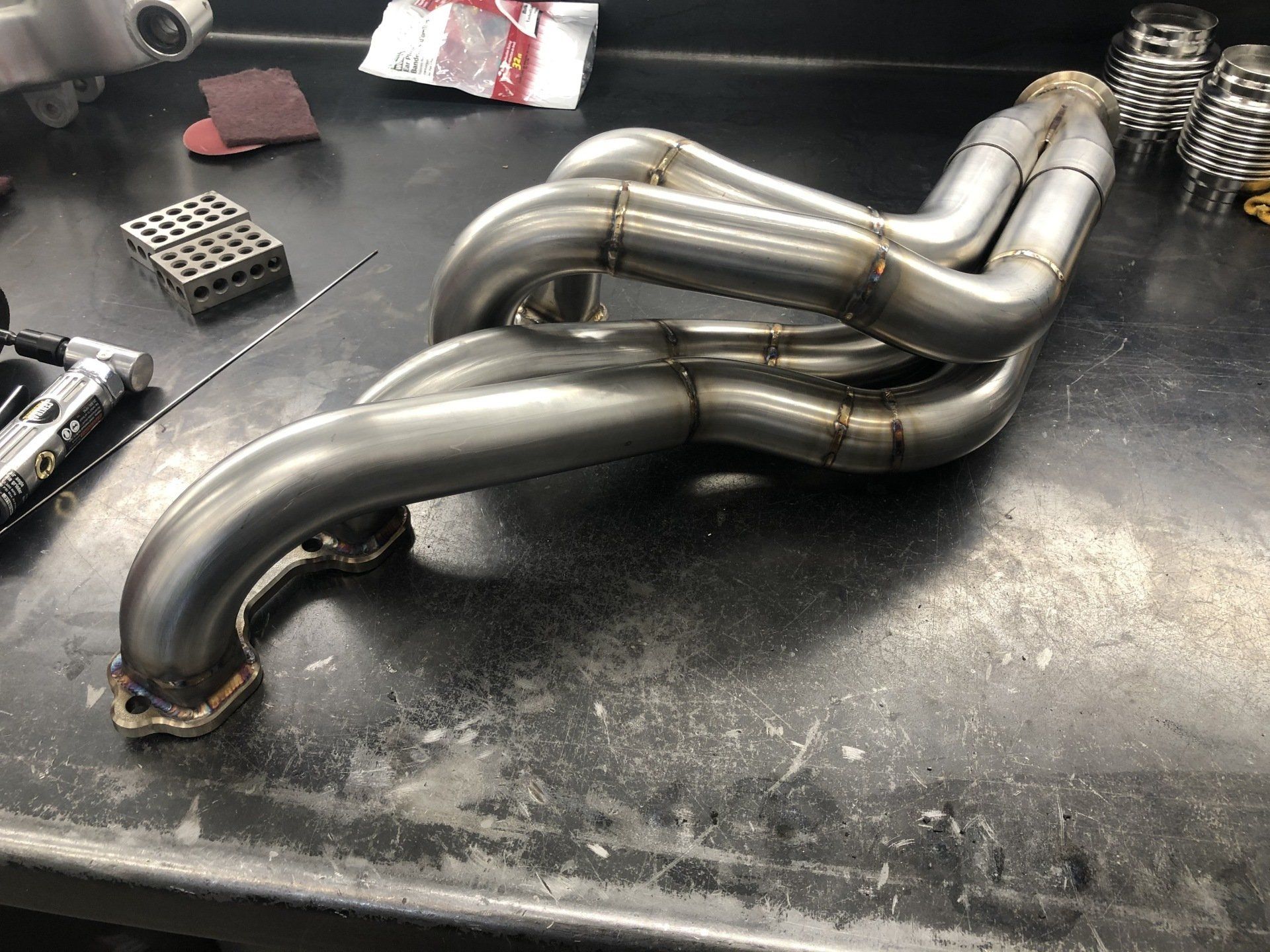 Stainless steel exhaust header pipes on a workbench in a workshop